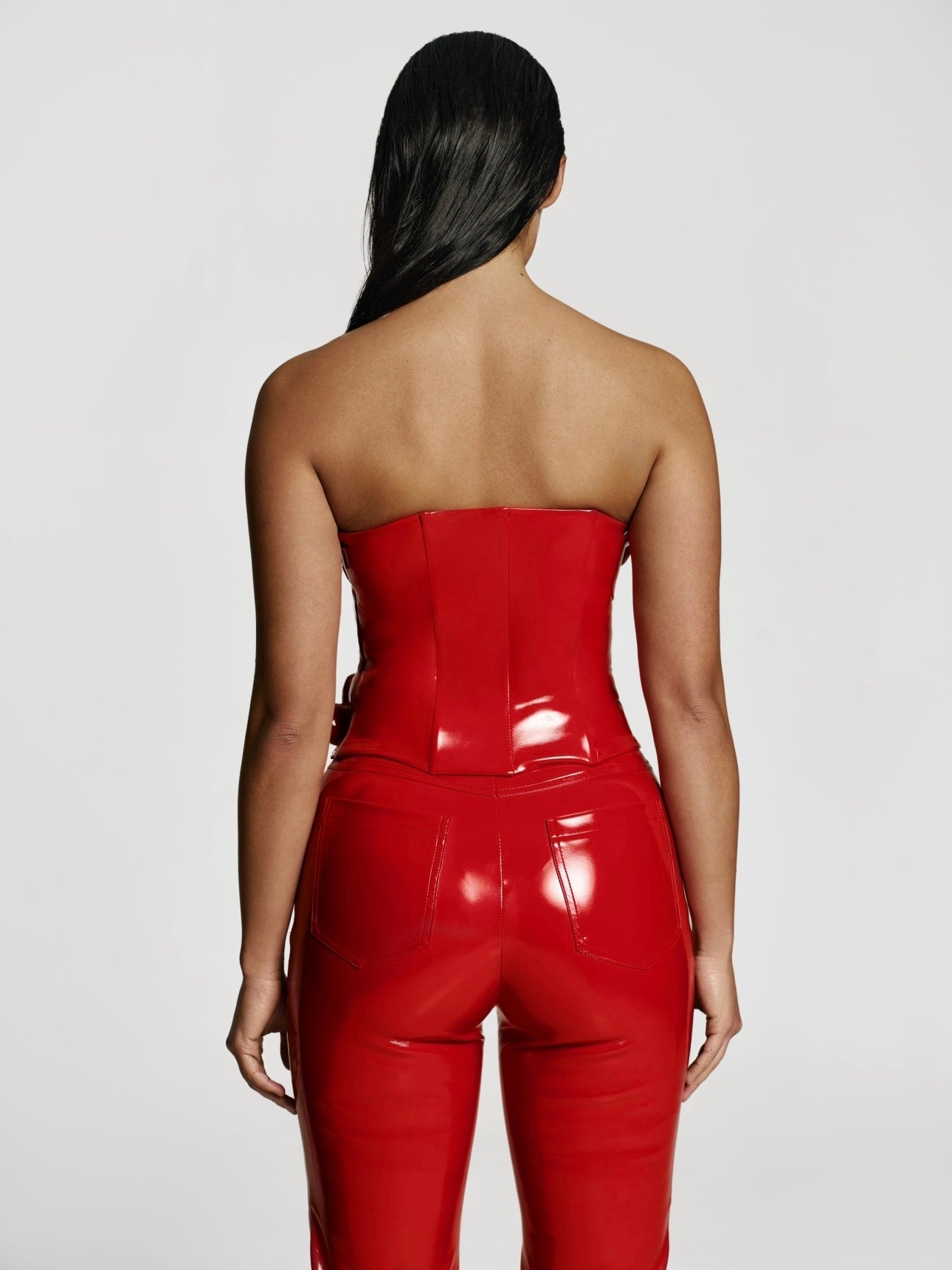 Cowboy shot of a girl facing back in a red patent vegan leather tube top and red patent vegan leather pants with straight leg