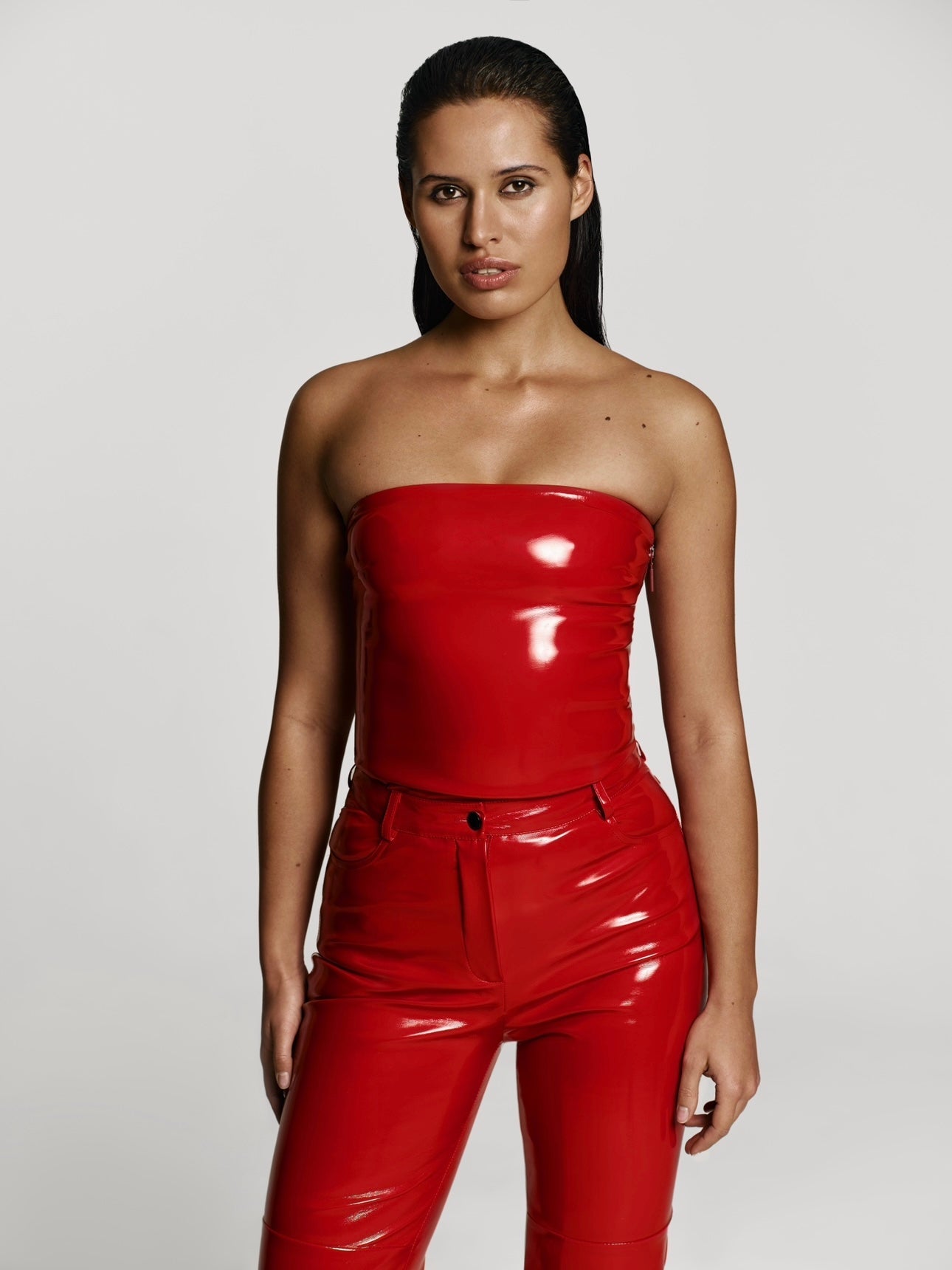Cowboy shot of a girl in a red patent vegan leather tube top and red patent vegan leather pants with straight leg