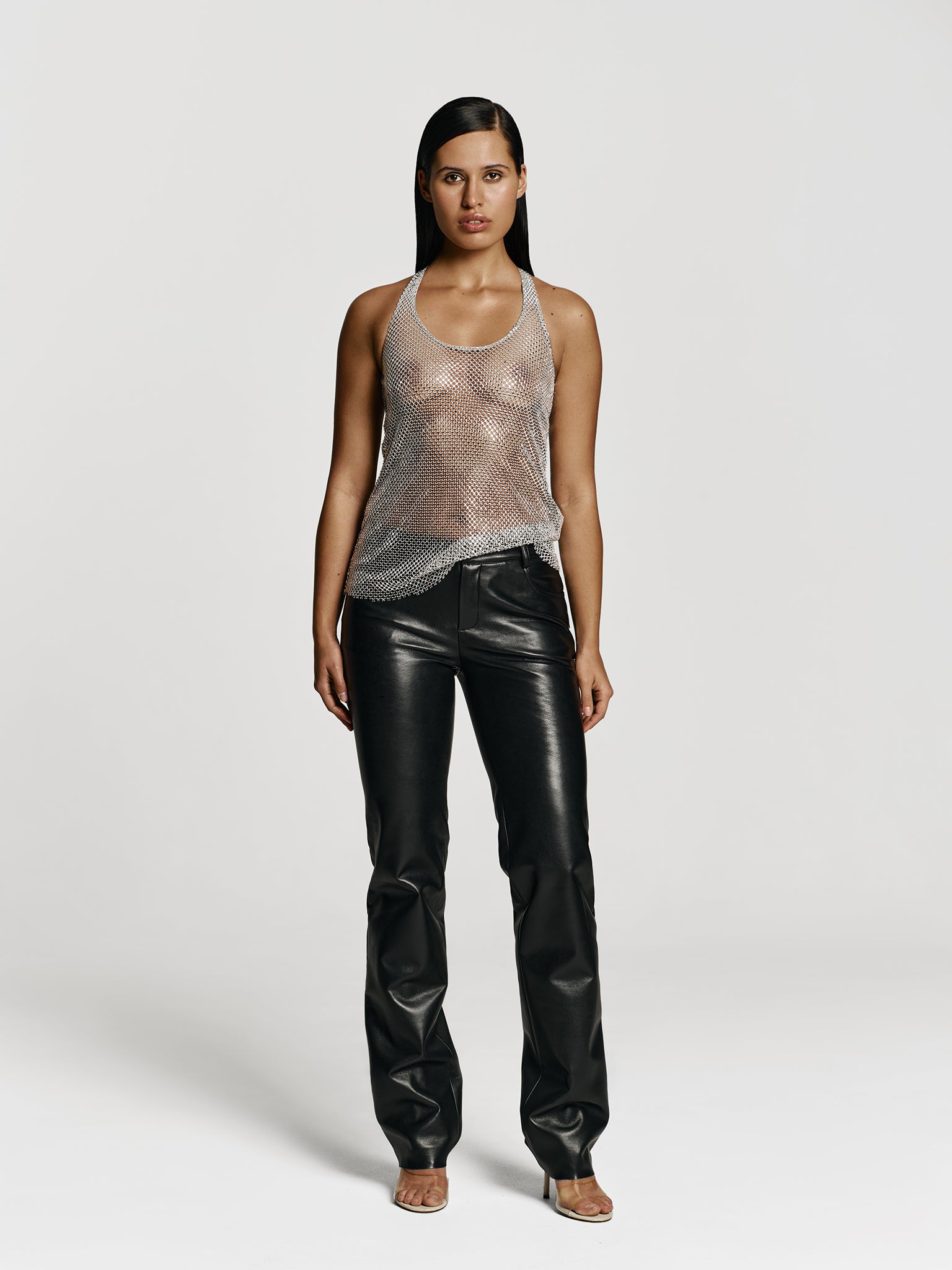 Full shot of a girl in a grey net tank top decorated with rhinestones and black leather medium rise straight leg pants