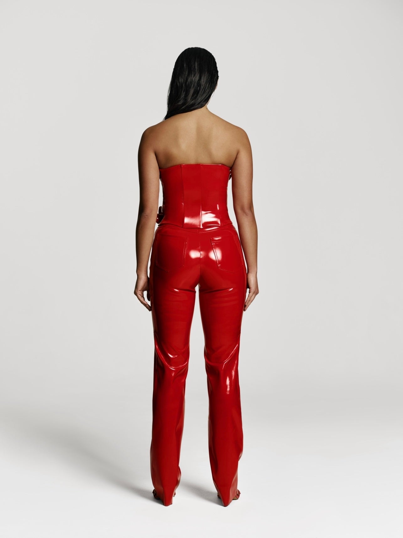 Full shot of a girl facing back in a red patent vegan leather tube top and red patent vegan leather pants with straight leg