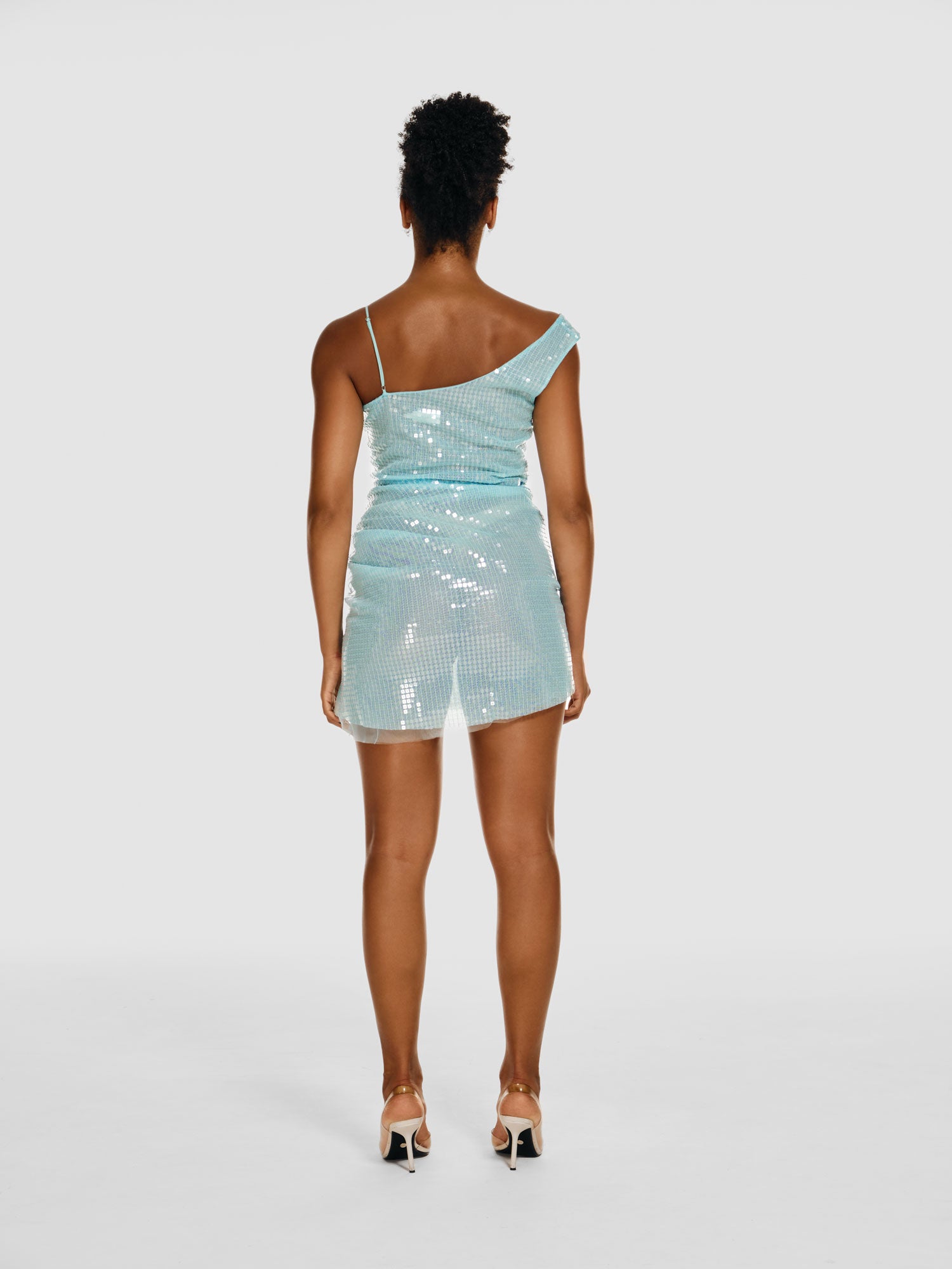 Full shot of a girl facing back in a light blue semi-transparent sequinned one shoulder mini dress