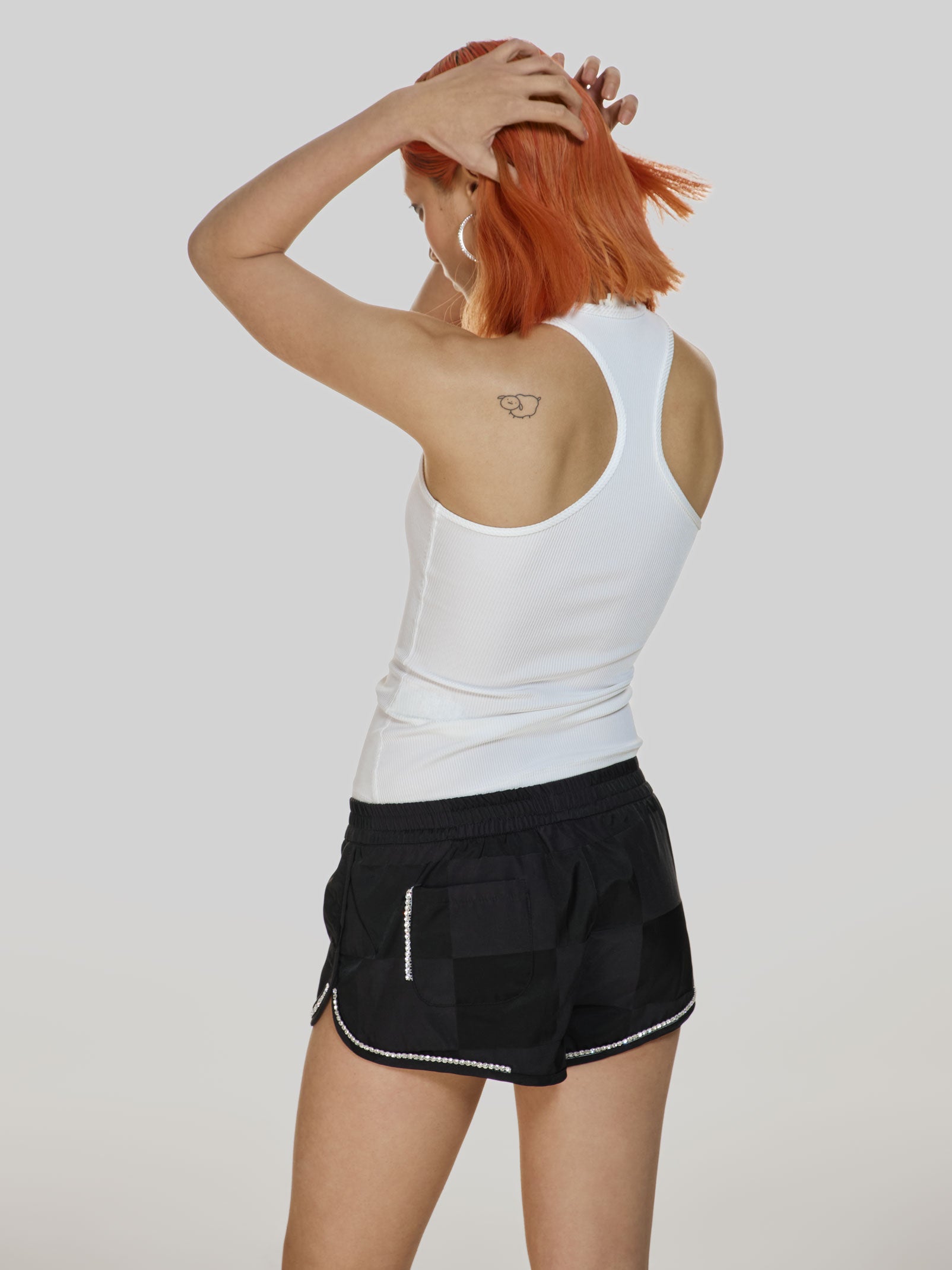 Cowboy shot of a girl facing back in a white viscose tank top and black checkered cotton shorts, decorated with rhinestones