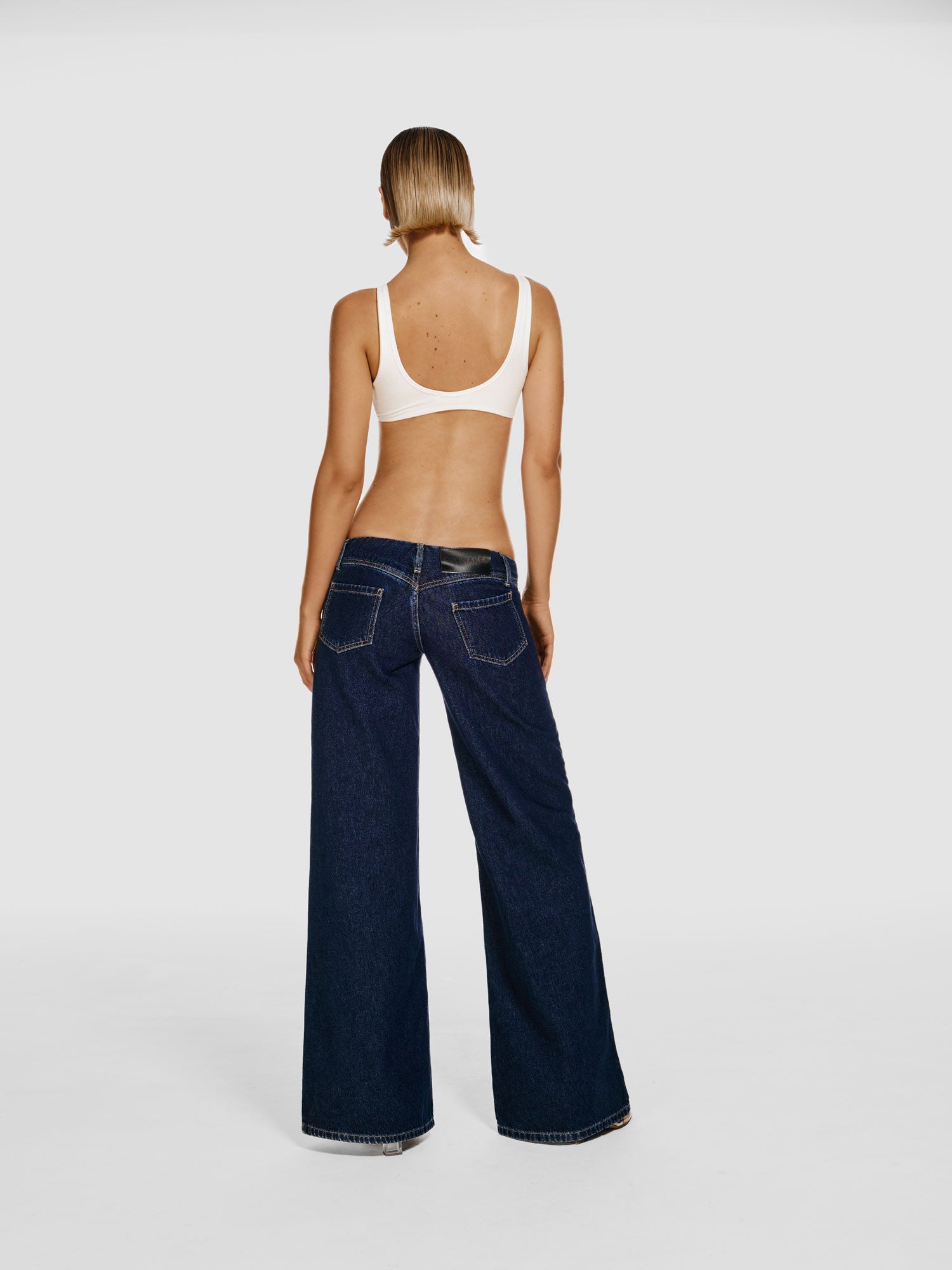 Full shot of a girl facing back in a white viscose crop top and blue wide leg jeans with low rise