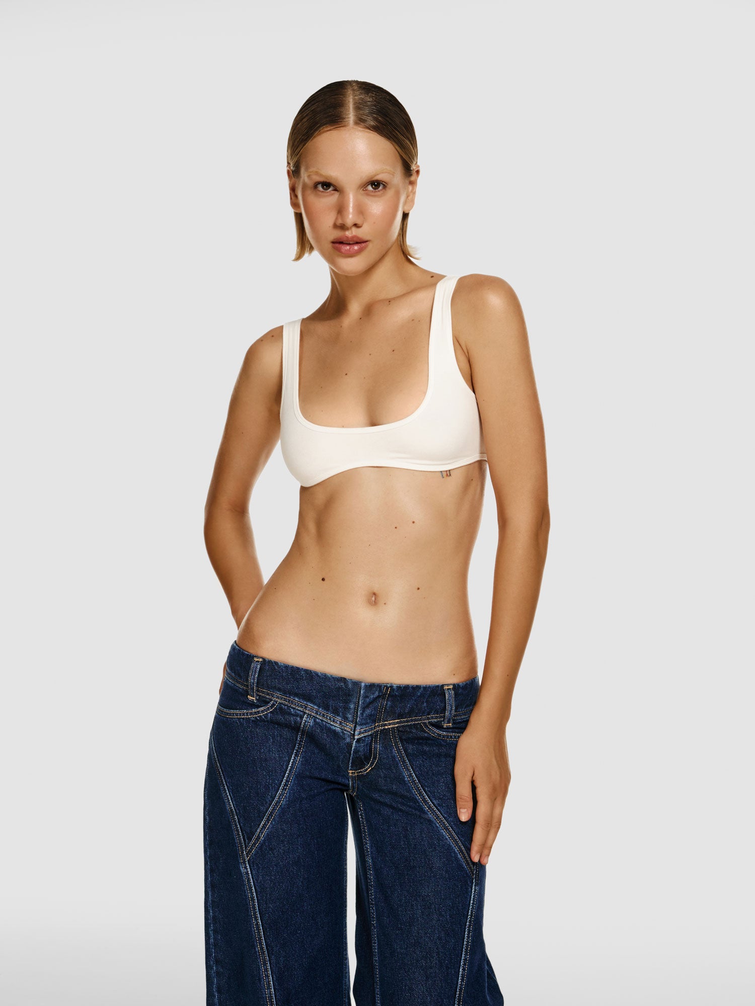Cowboy shot of a girl in a white viscose crop top and blue wide leg jeans with low rise
