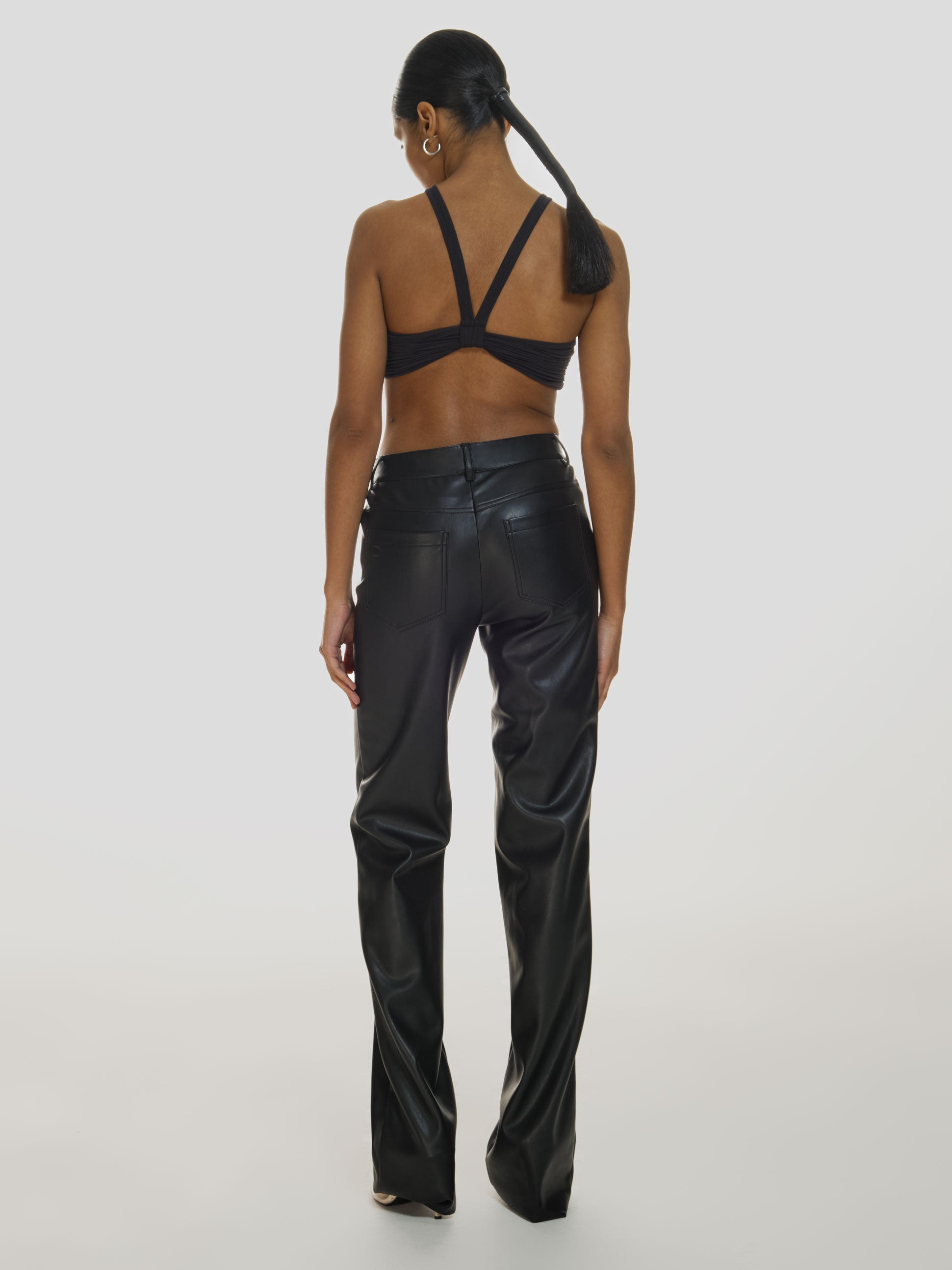 Full shot of a girl facing back in a black crop top and black genuine leather pants with mid rise