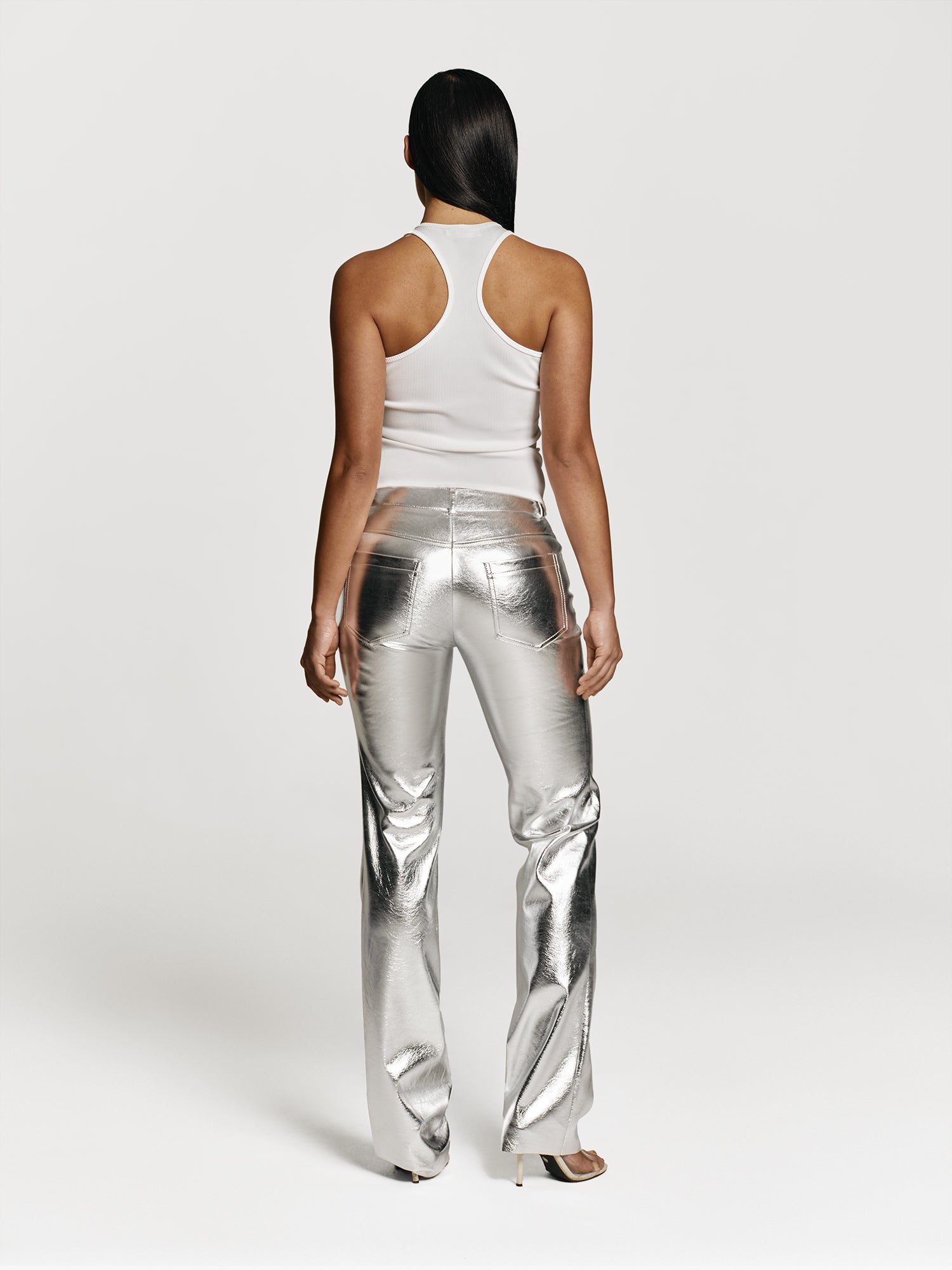 Full shot of a girl in a white viscose tank top and silver straight leg pants with mid rise