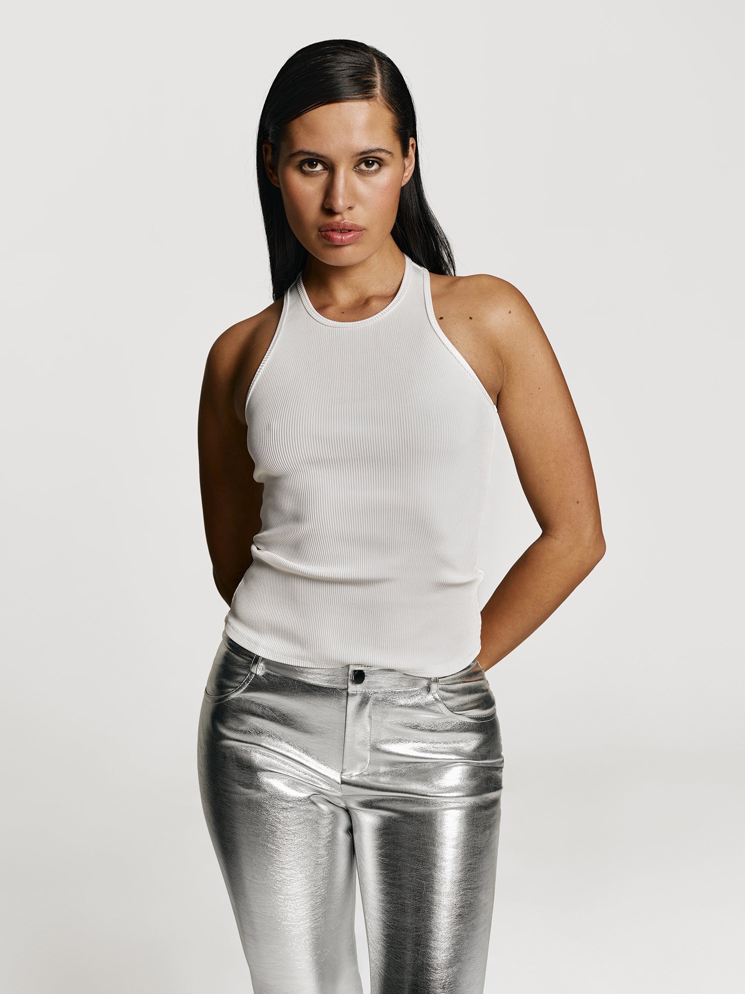 Cowboy shot of a girl in a white viscose tank top and silver straight leg pants with mid rise