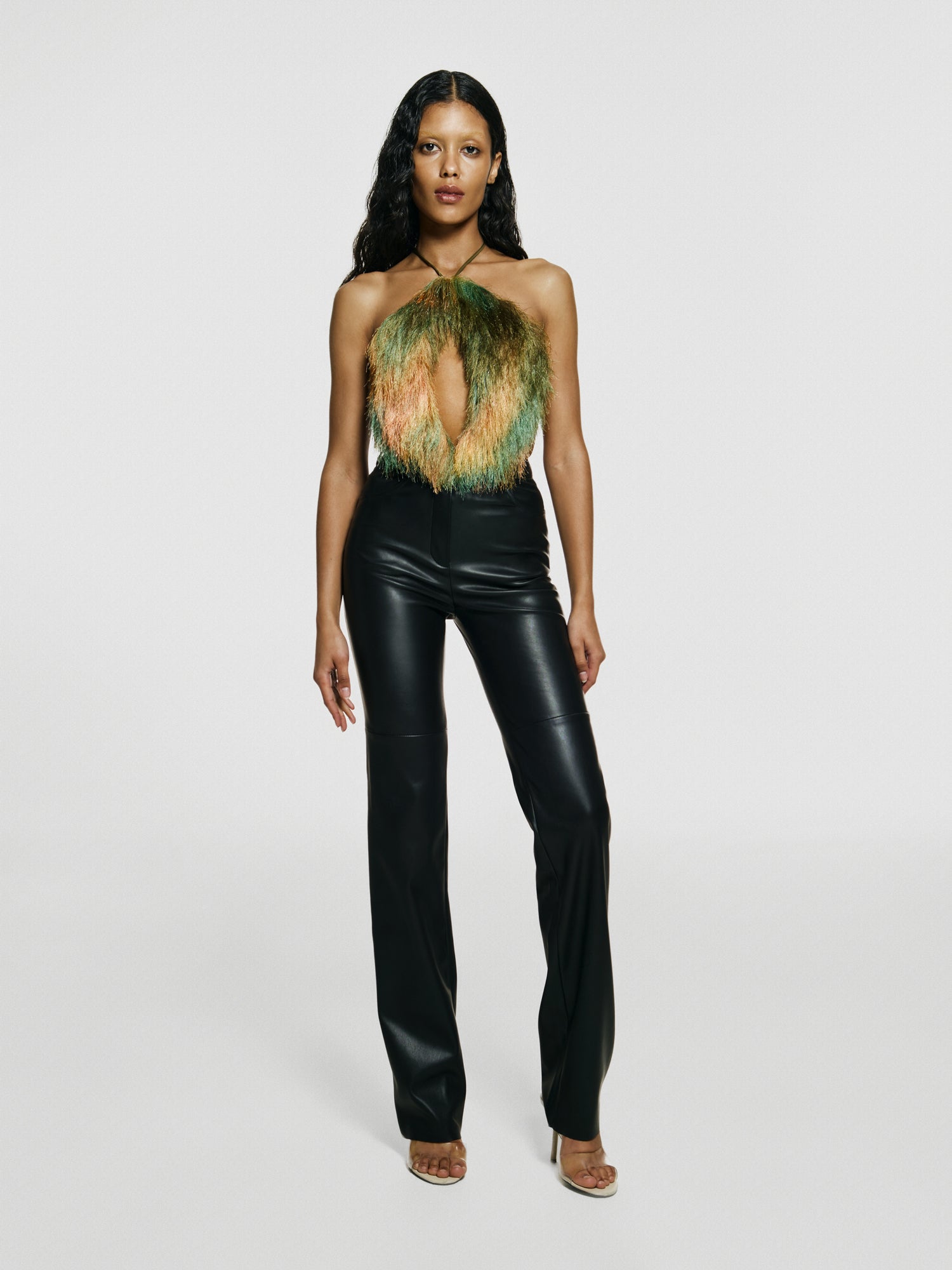 Medium full shot of a girl in a green opened back sleeveless bodysuit with a vertical cut in front and black leather high rise straight leg pants