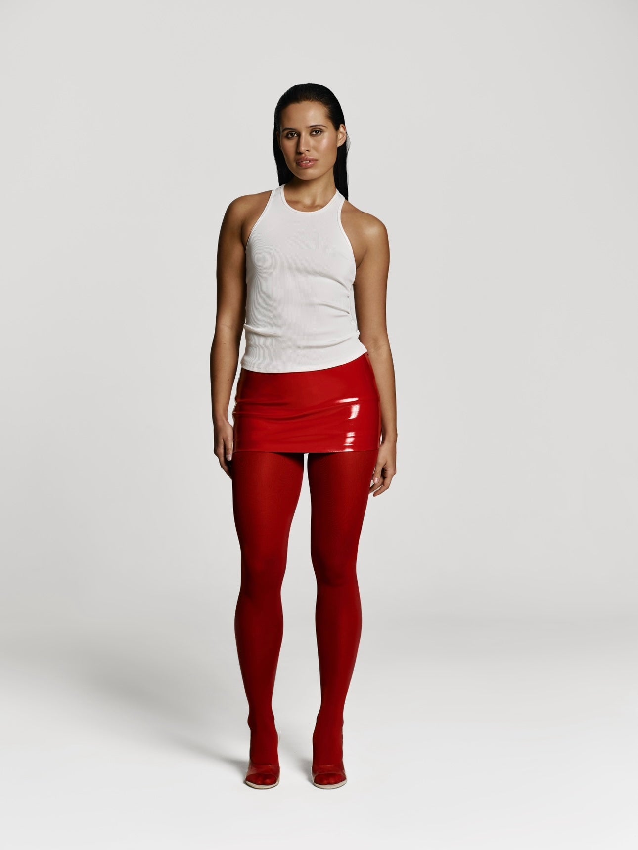 Full shot of a girl in a a white viscose tank top, a red patent vegan leather mini skort and red tights