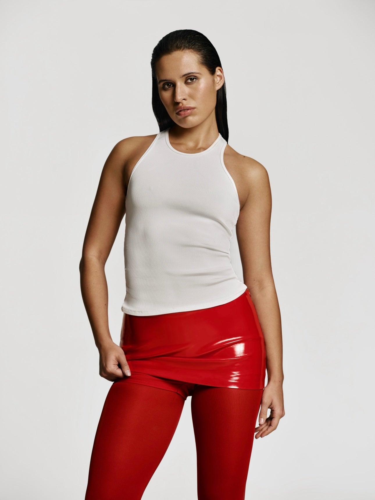 Medium full shot of a girl in a white viscose top, a red patent vegan leather mini skort and red tights