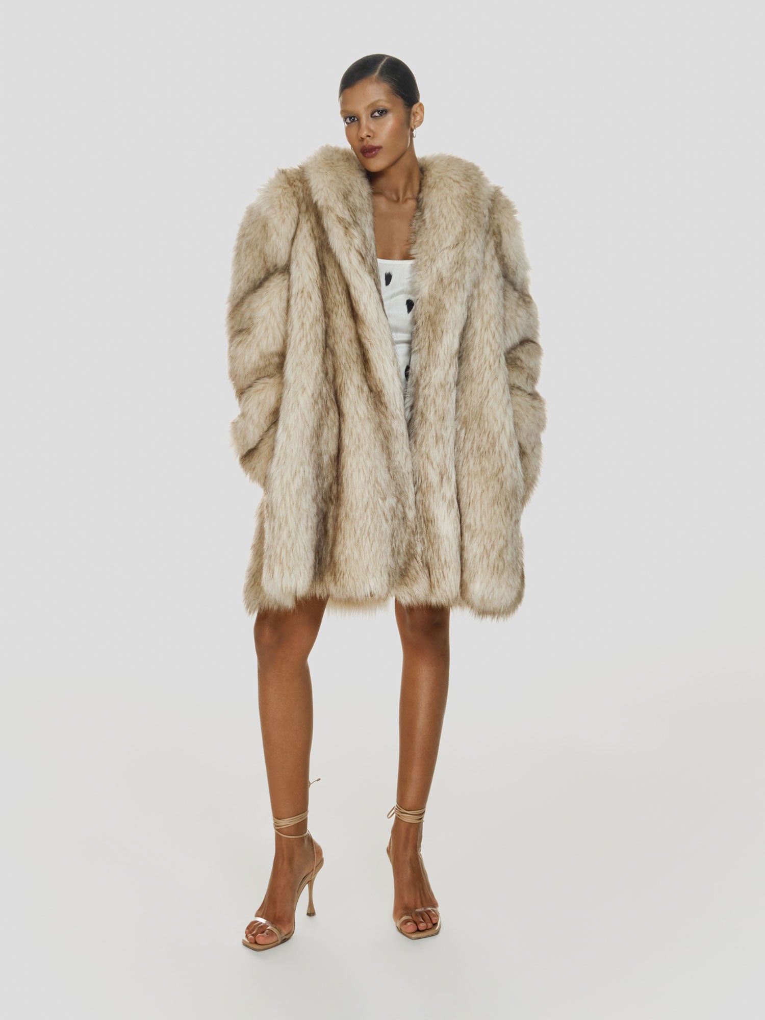 Full shot of a girl in a medium length oversized eco fur coat and white cotton mini tank dress