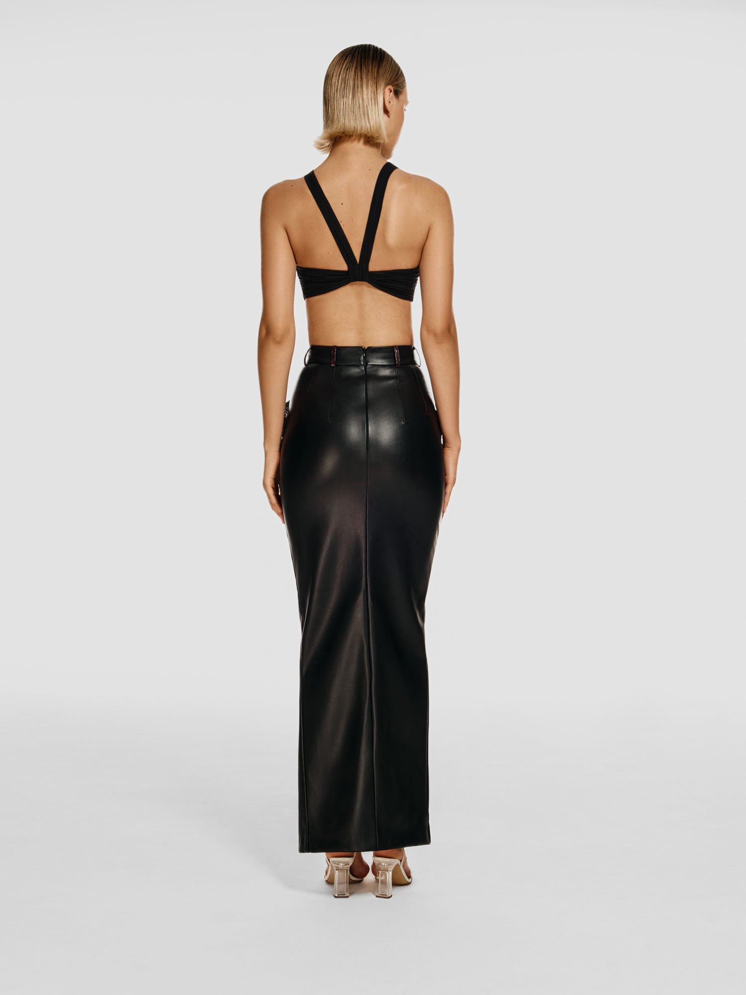 Full shot of a girl facing back in a black viscose crop top and a black vegan leather maxi skirt with a high front slit