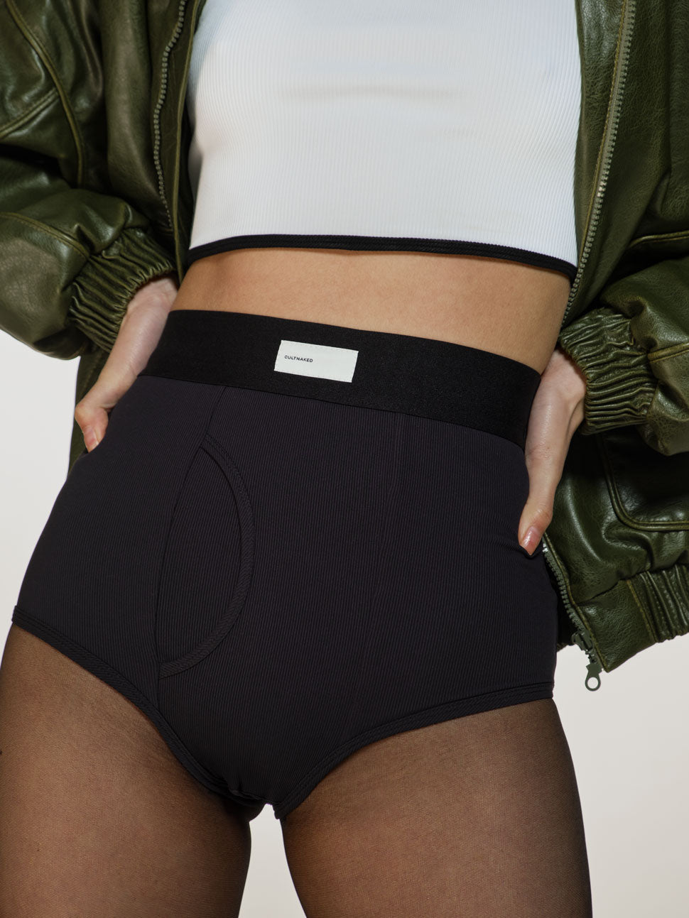 Medium closeup shot of a girl in a white viscose crop top, black viscose briefs with high rise, green vegan leather bomber and black sheer tights