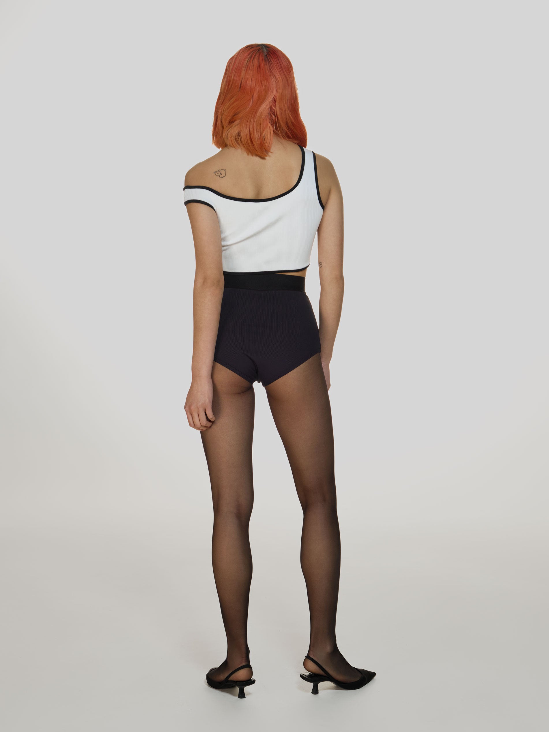 Full shot of a girl facing back in a white viscose crop top, black viscose high rise briefs and black tights