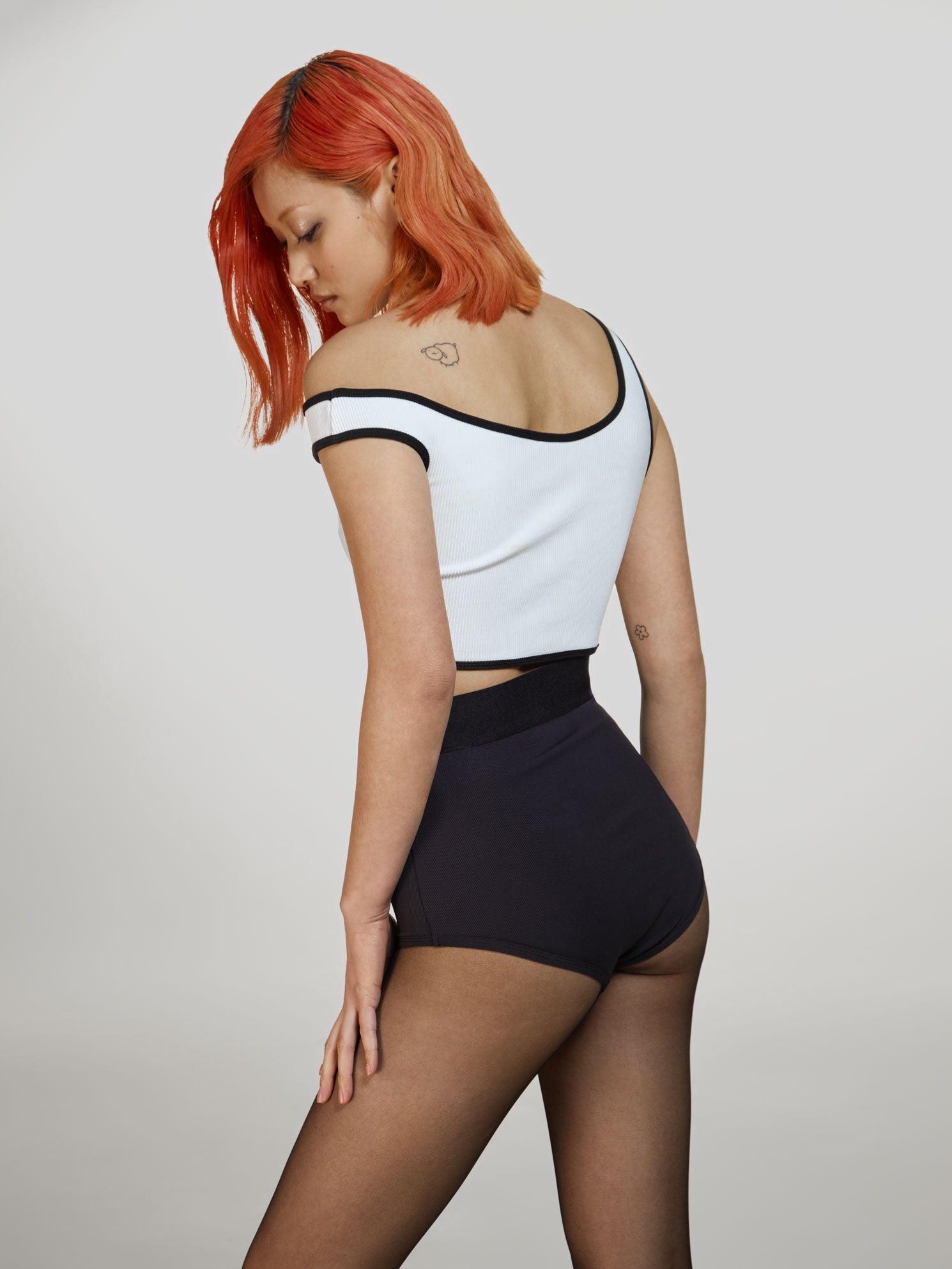 Medium full shot of a girl facing back in a white viscose crop top, black viscose briefs with high rise and black sheer tights