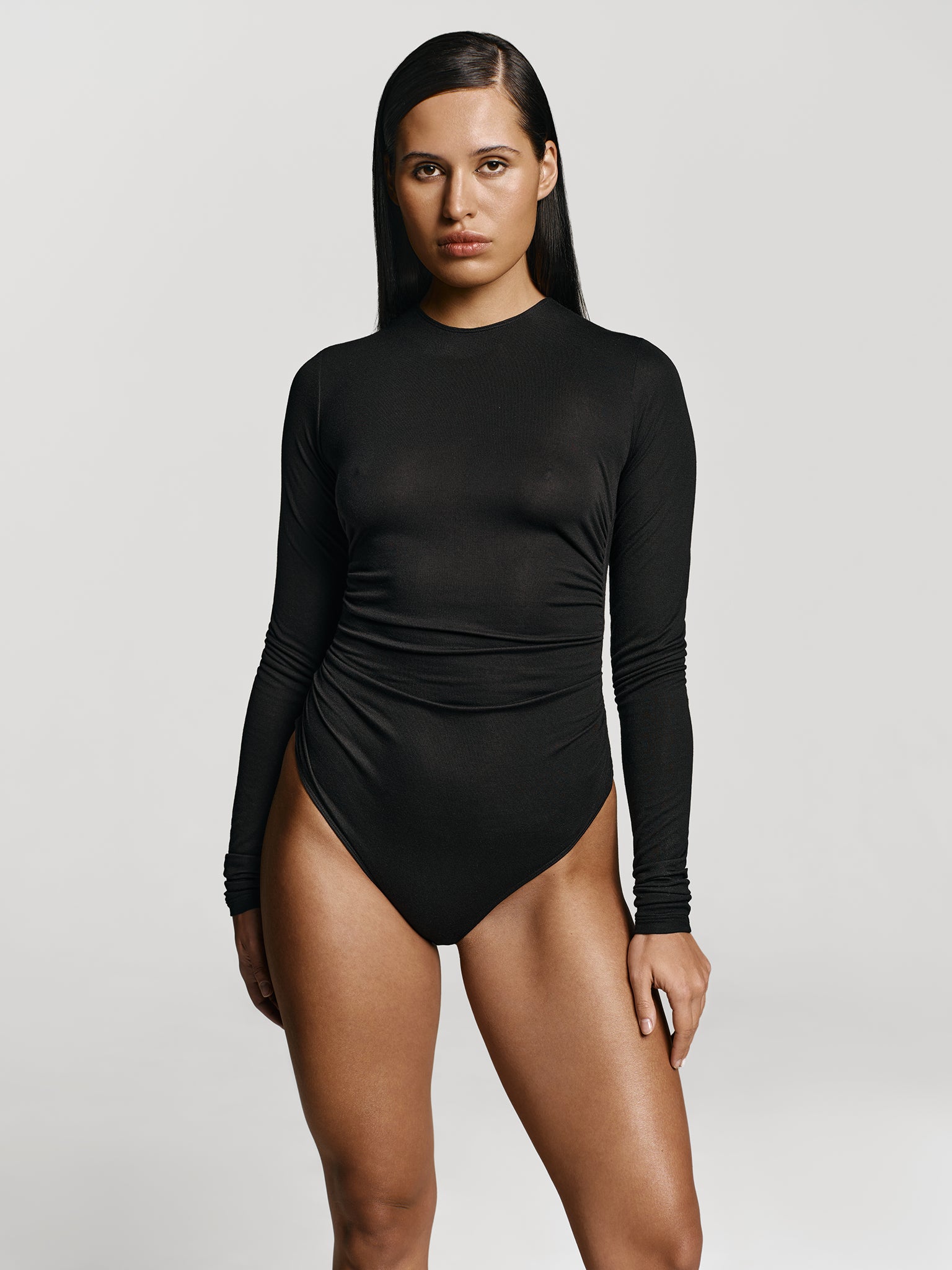 Medium full shot of a girl in a black long sleeved bodysuit with draping at the sides and high round neckline