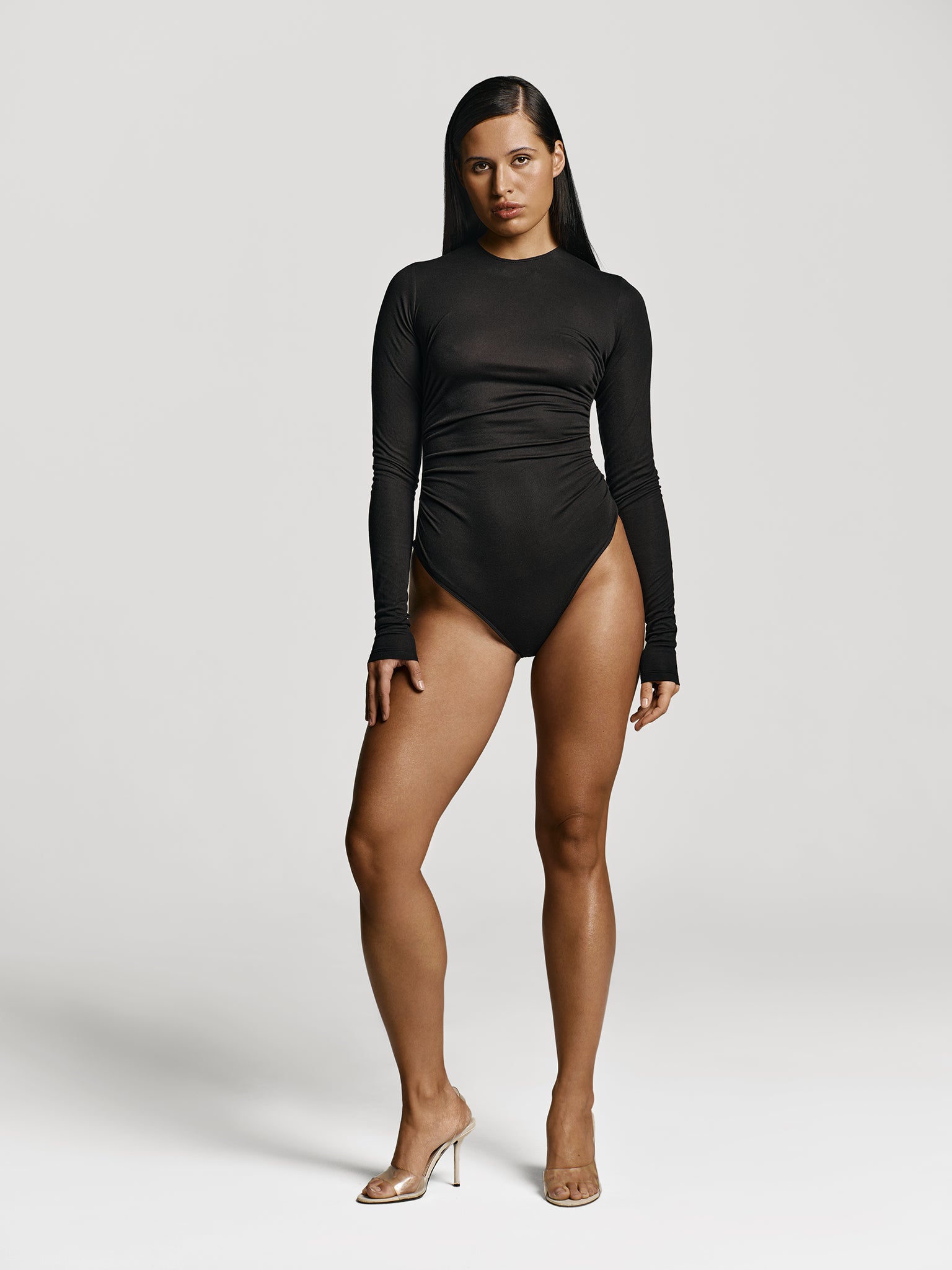 Full shot of a girl in a black long sleeved bodysuit with draping at the sides and high round neckline