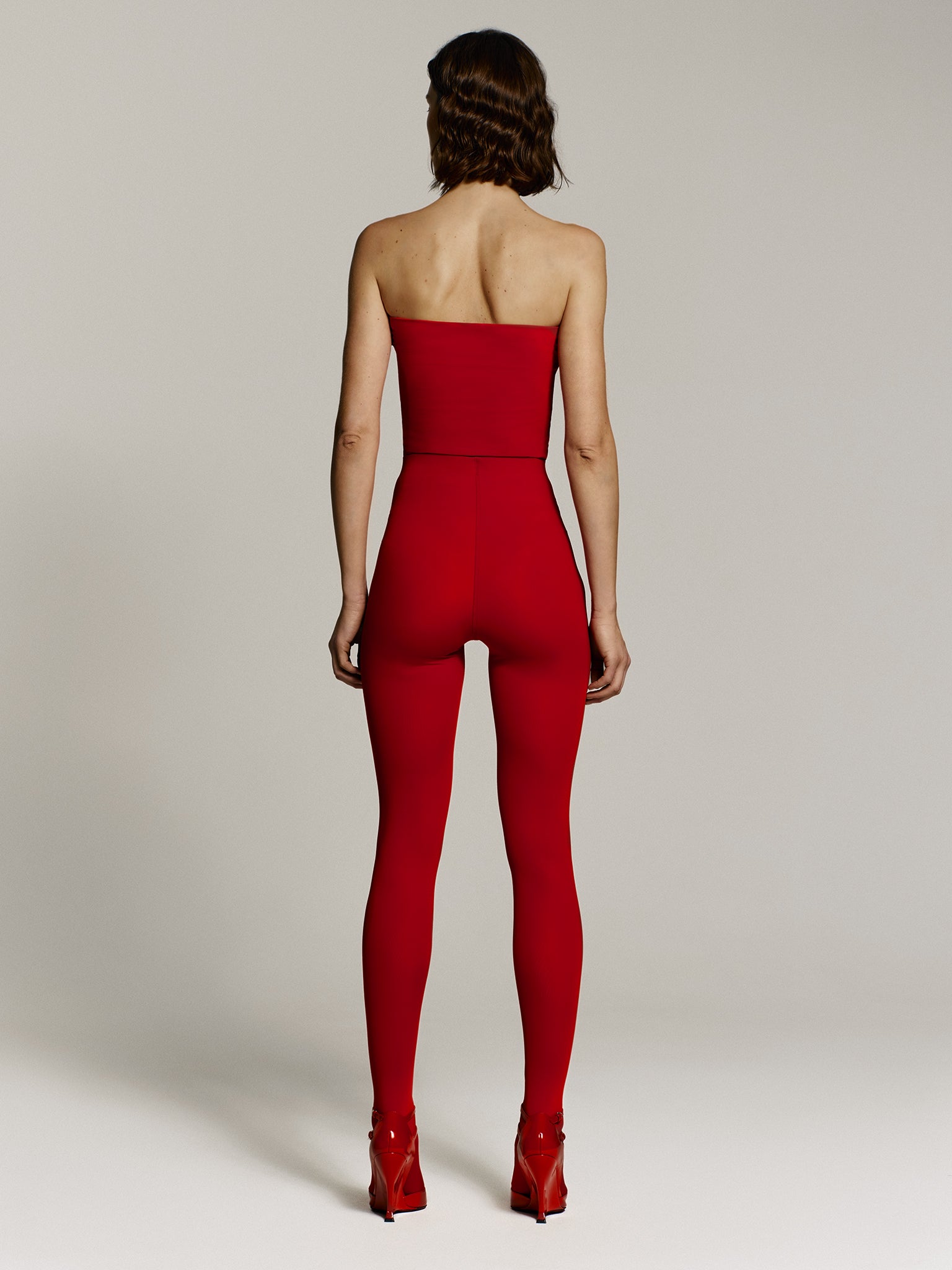 Full shot of a girl facing back in a red regenerated plastic tube top and red regenerated plastic high rise leggings