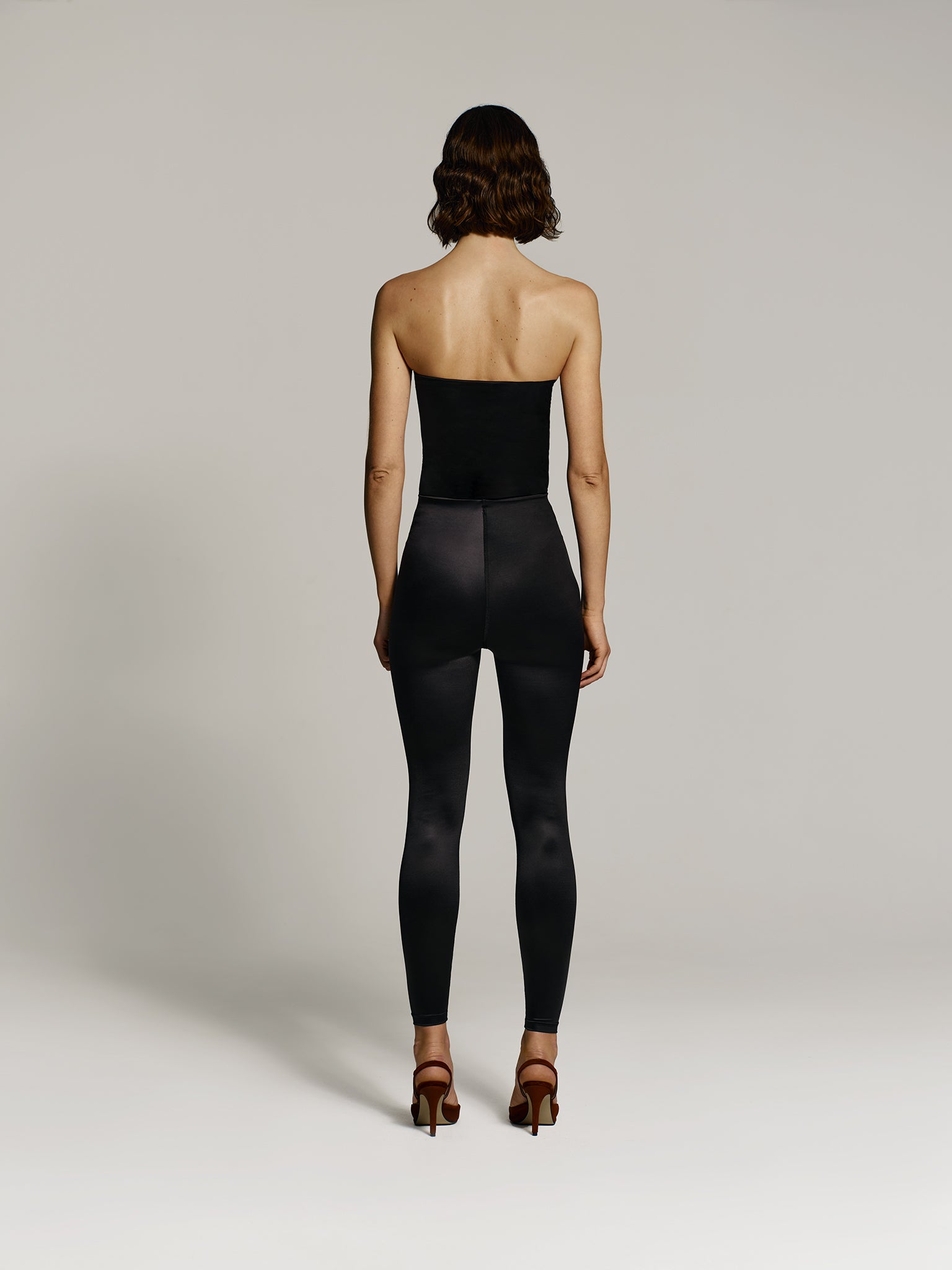 Full shot of a girl facing back in a black regenerated plastic tube top and black regenerated plastic high rise leggings