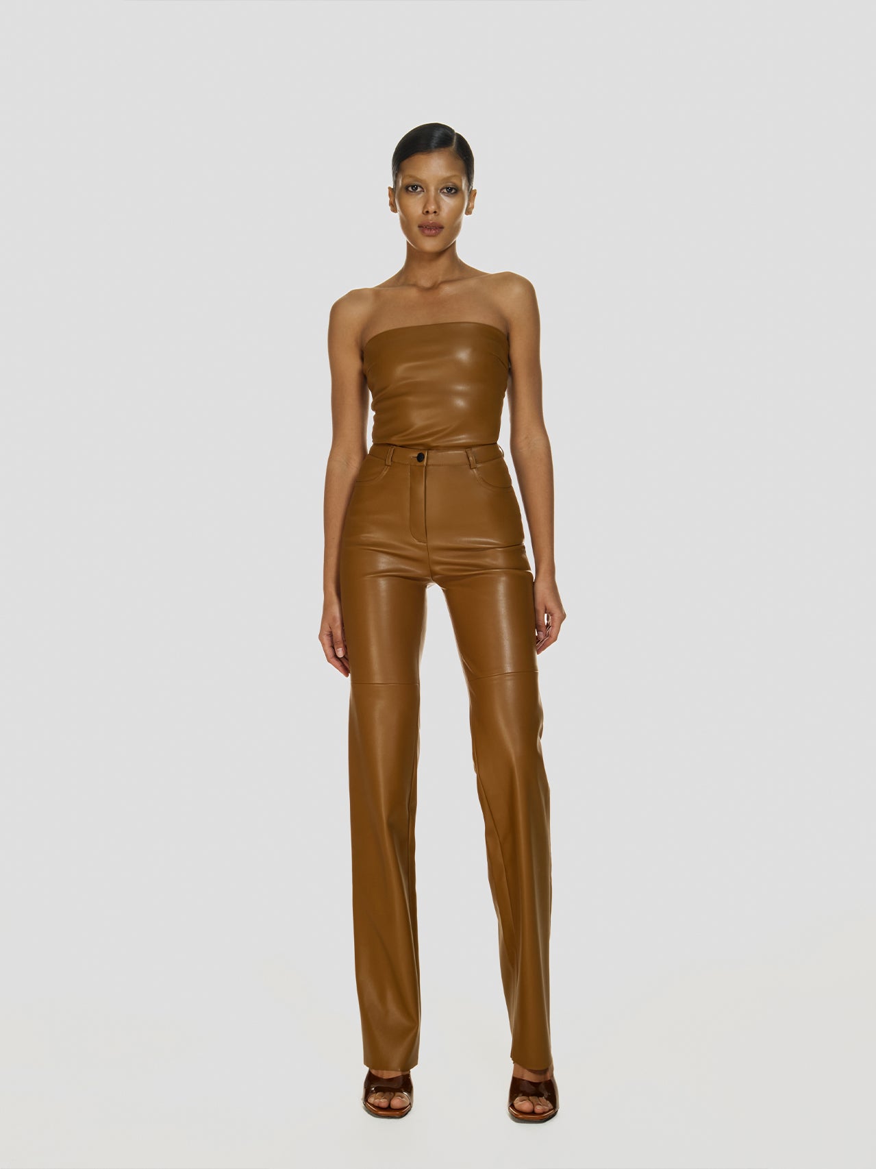 Full shot of a girl in a brown vegan leather tube top and brown vegan leather high rise pants with straight leg