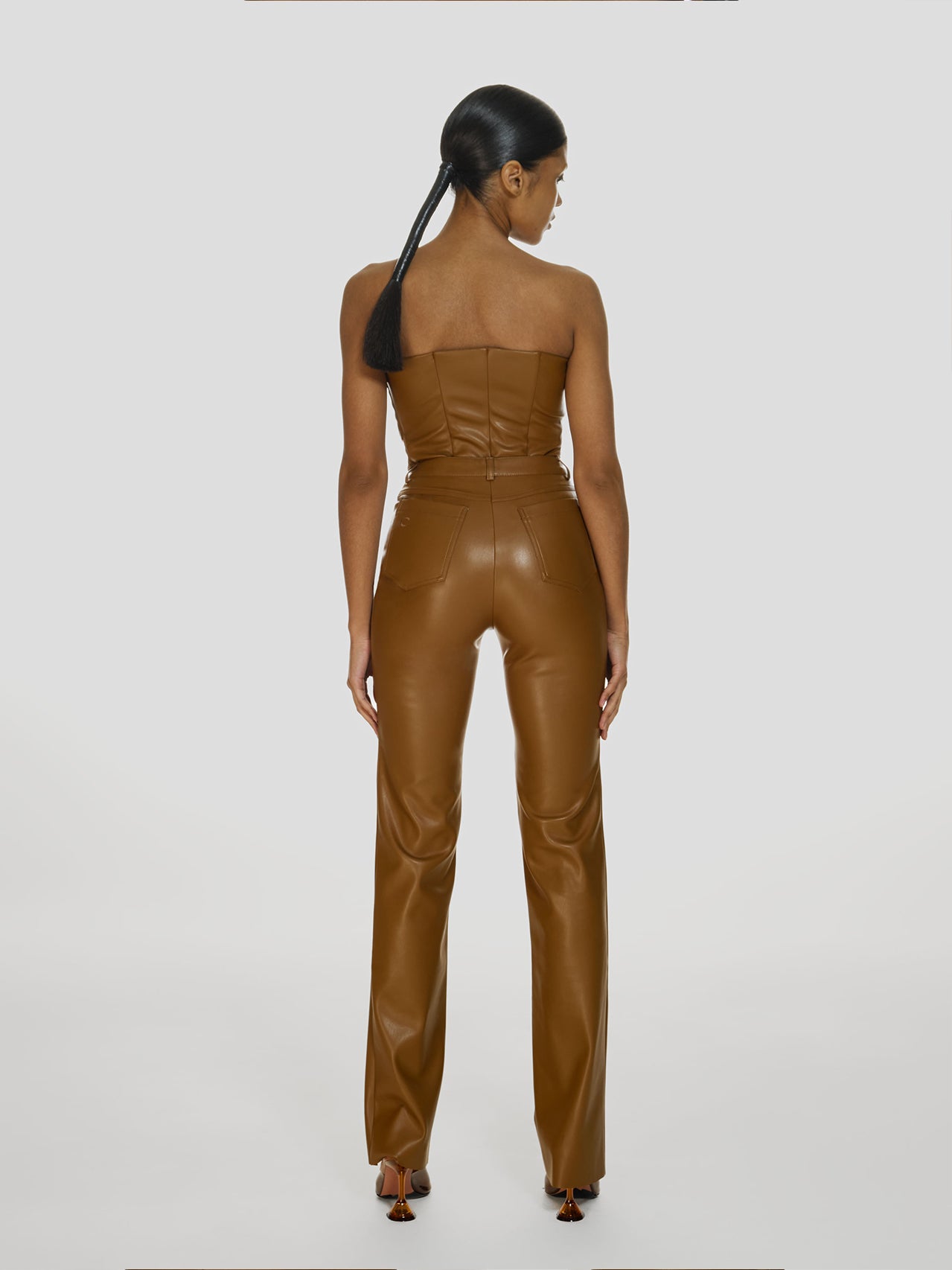Full shot of a girl in a brown vegan leather tube top and brown vegan leather pants with straight leg
