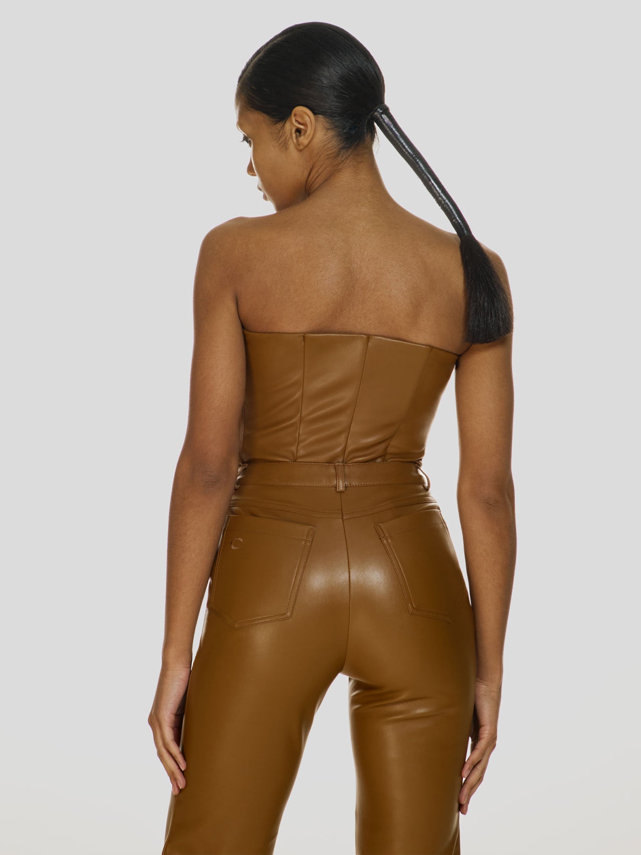 Cowboy shot of a girl in a brown vegan leather tube top and brown vegan leather high rise straight leg pants