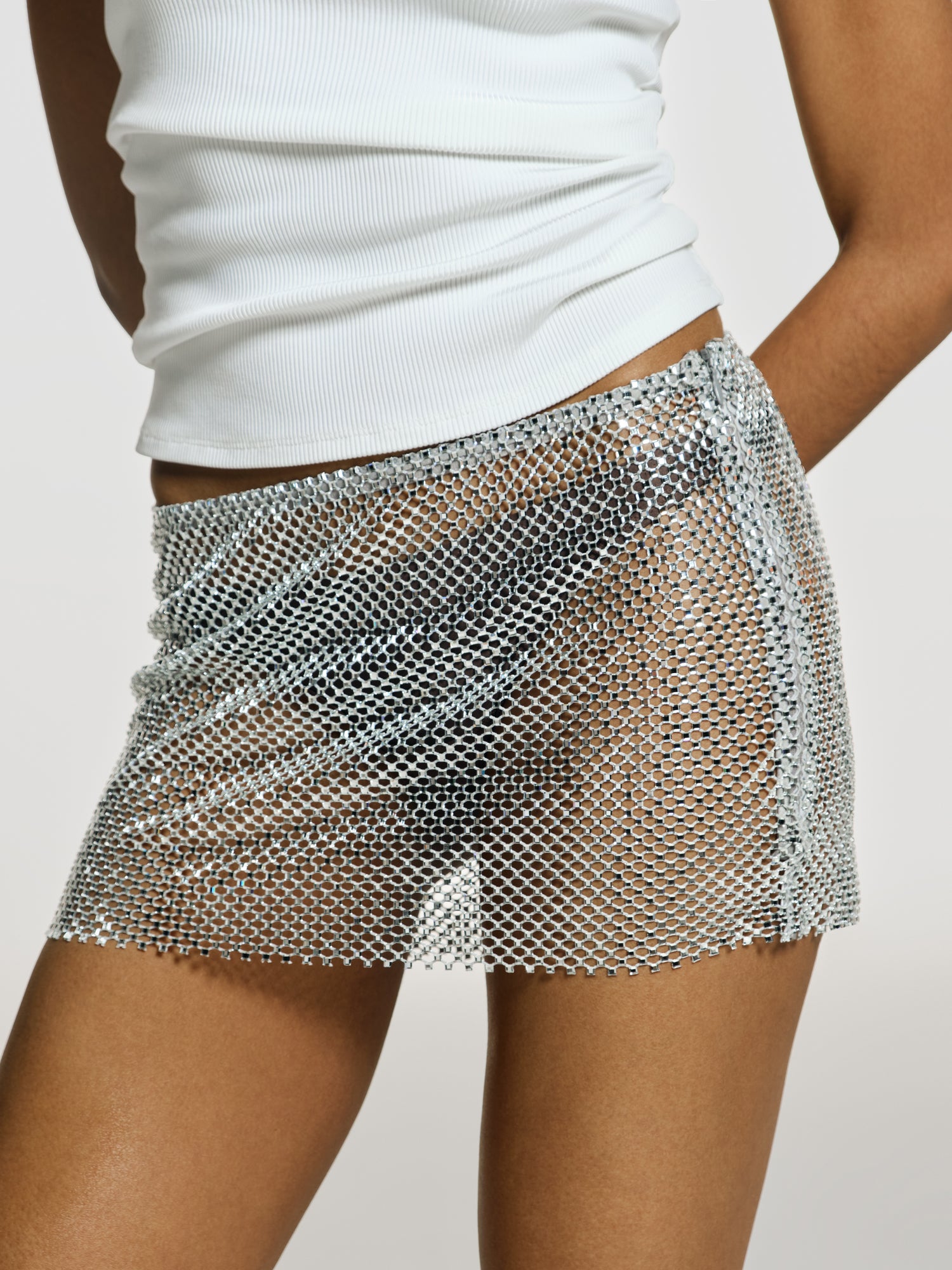 Closeup shot of a girl in a white viscose tank top and a grey net mini skirt decorated with rhinestones