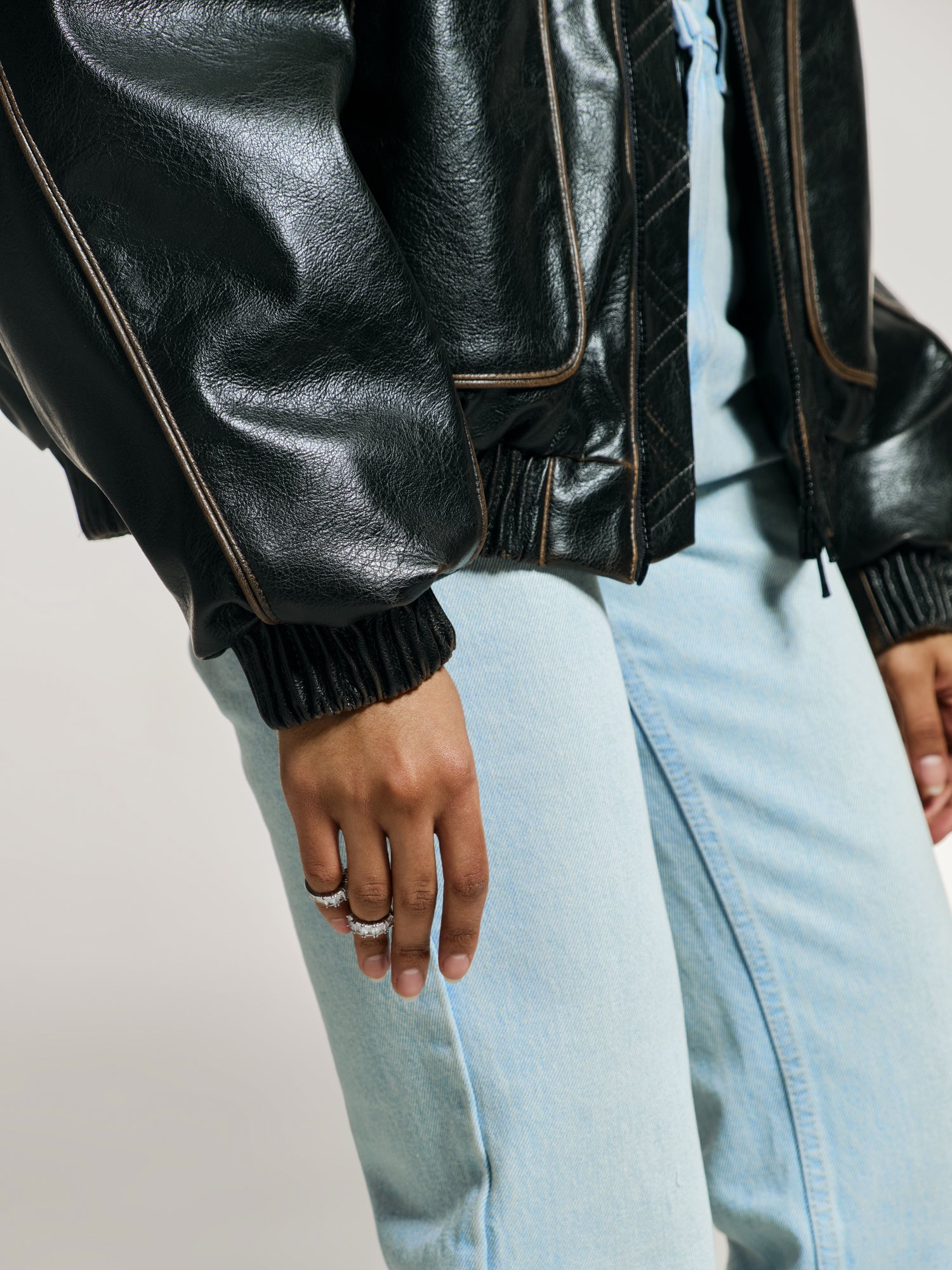 Closeup shot of a girl in a brown vegan leather oversized bomber and blue high rise jeans with a straight leg