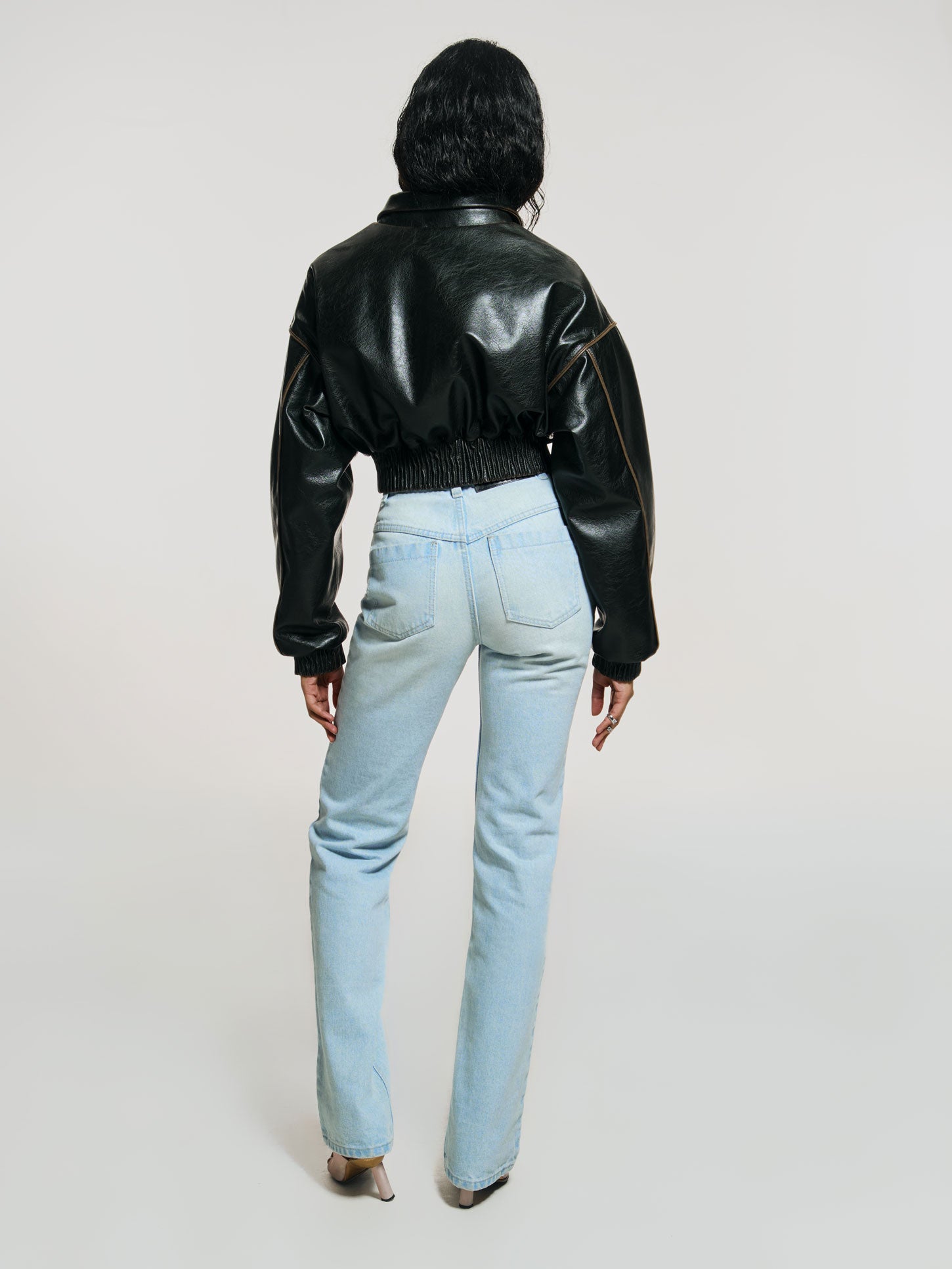 Full shot of a girl facing back in a brown vegan leather oversized cropped bomber and blue high rise jeans with straight leg