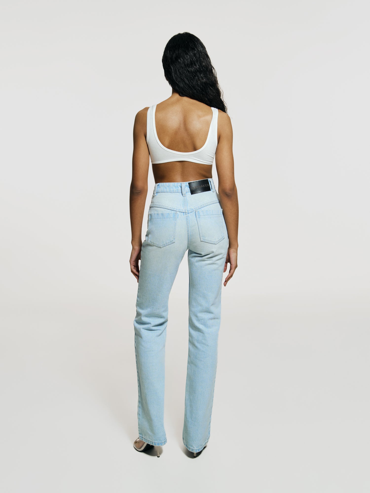 Full shot of a girl facing back in white viscose crop top and in blue high rise straight leg jeans