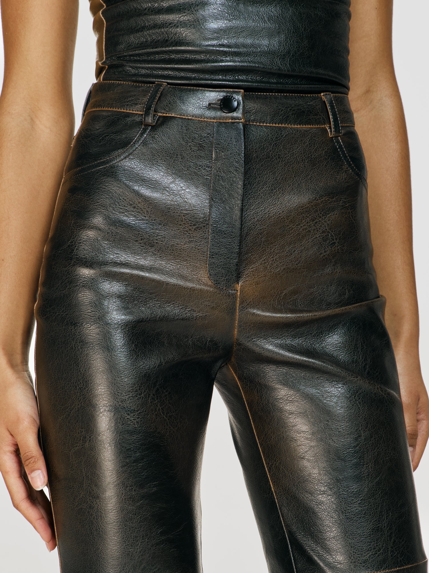 Medium closeup shot of a girl in a brown vegan leather tube top and brown vegan leather high rise straight leg pants