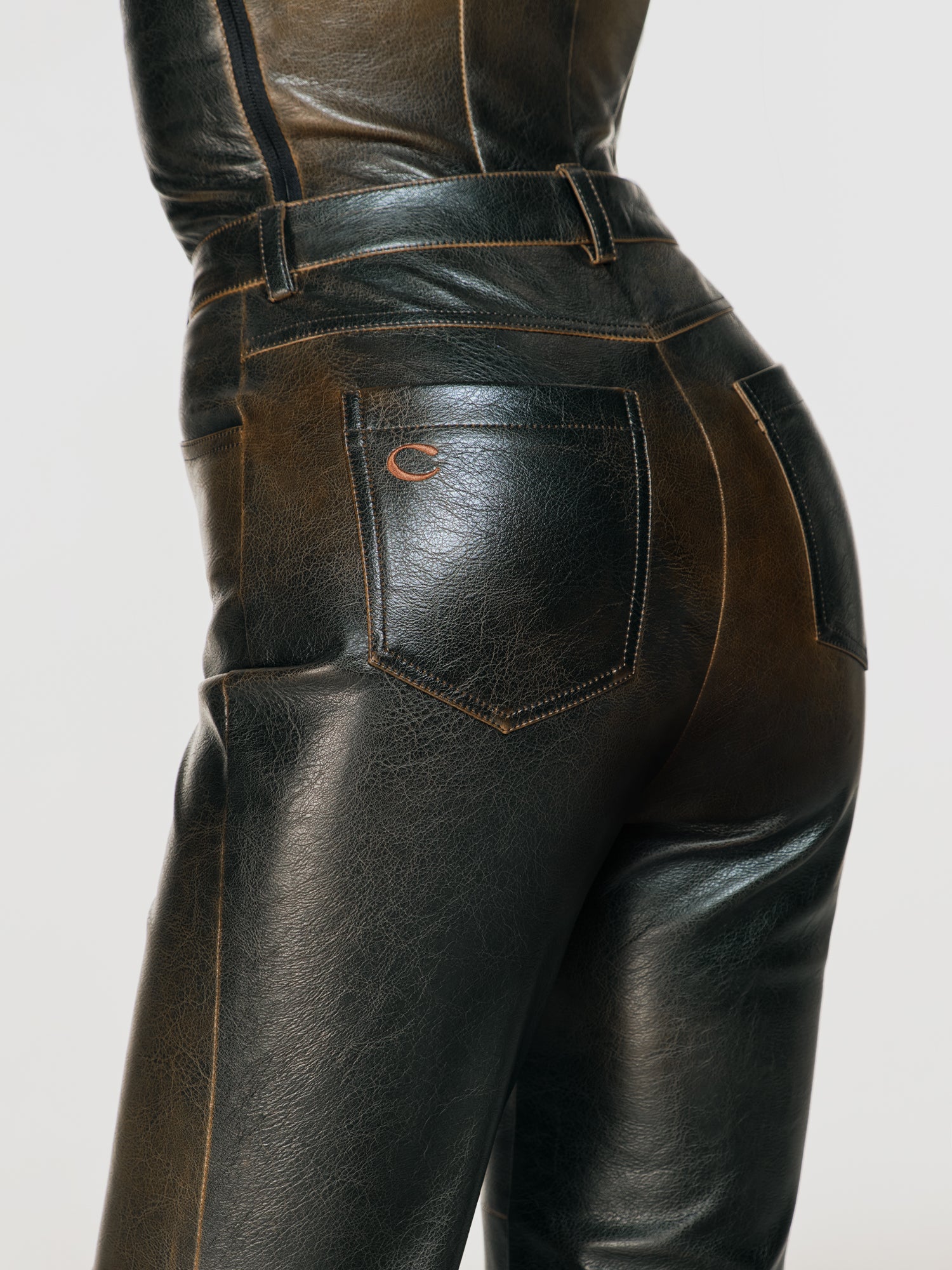 Closeup shot of a girl facing back in a brown vegan leather tube top and brown vegan leather high rise pants with straight leg