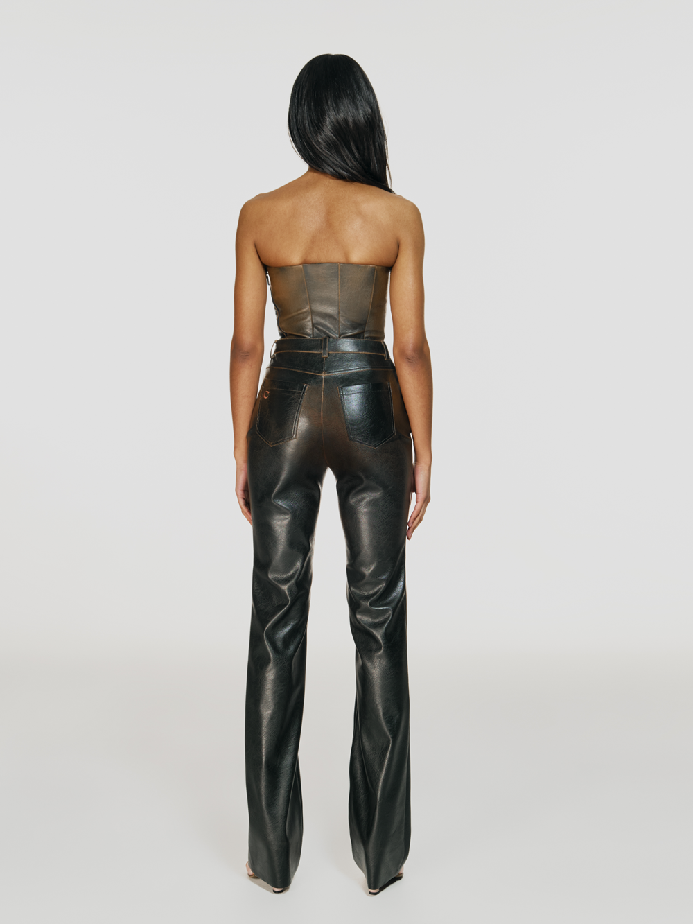 Full shot of a girl facing back in a brown vegan leather tube top and brown vegan leather pants with straight leg