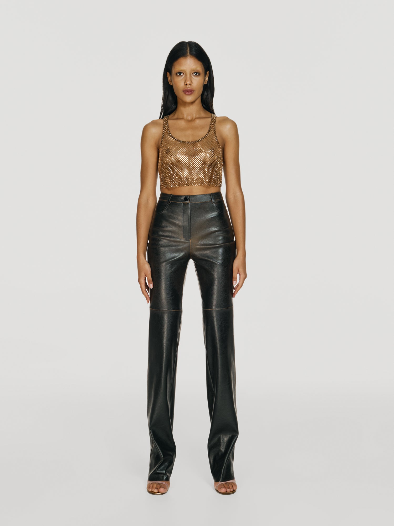 Full shot of a girl in a brown net croppped tank top decorated with rhinestones and brown vegan leather high rise straight leg pants