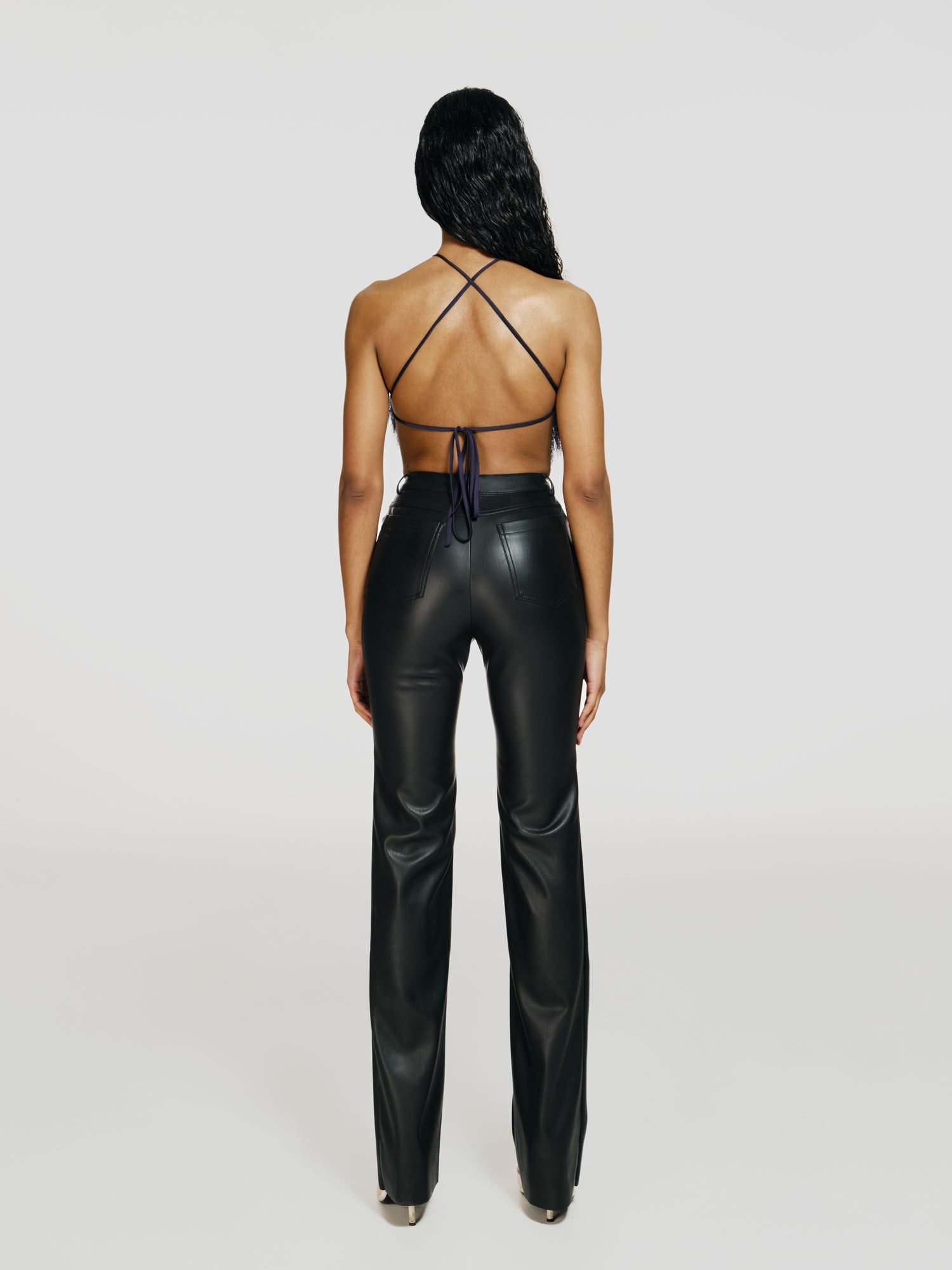 Full shot of a girl facing back in a purple opened back sleeveless bodysuit with a vertical cut in front and black leather high rise straight leg pants