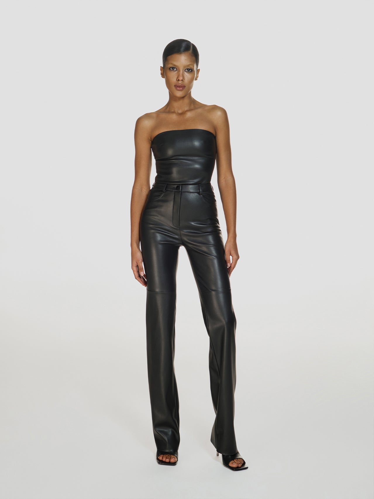 Full shot of a girl in a black vegan leather tube top and black vegan leather high rise pants with straight leg
