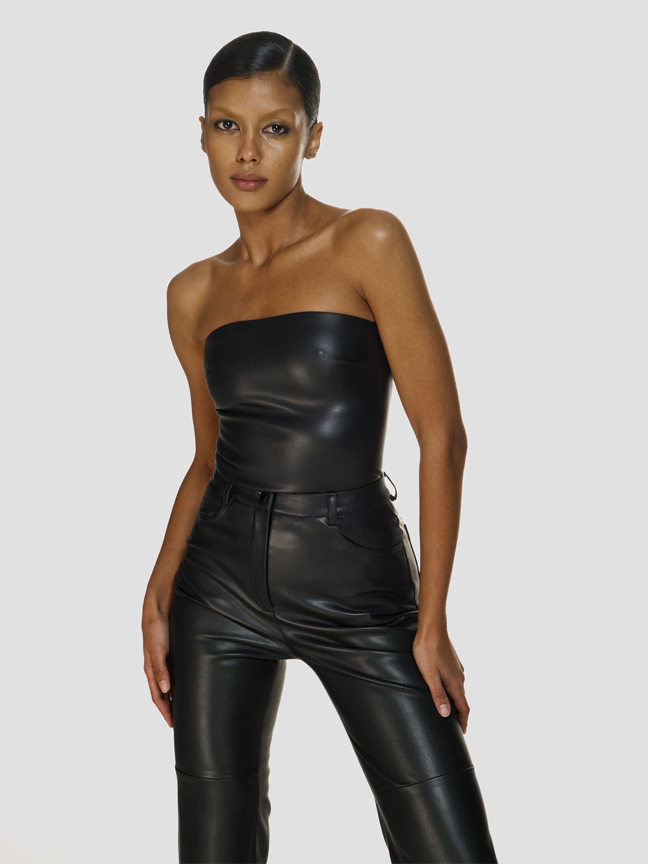 Medium full shot of a girl in a black vegan leather tube top and black vegan leather high rise pants with straight leg
