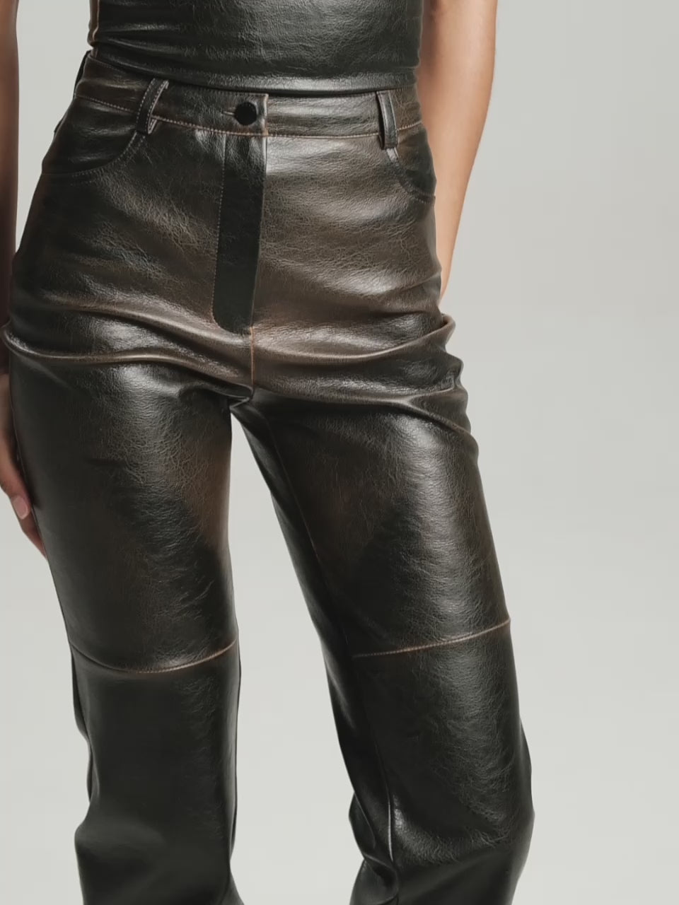 Video of a medium closeup and closeup shot of a girl in a brown vegan leather tube top and brown vegan leather pants with straight leg