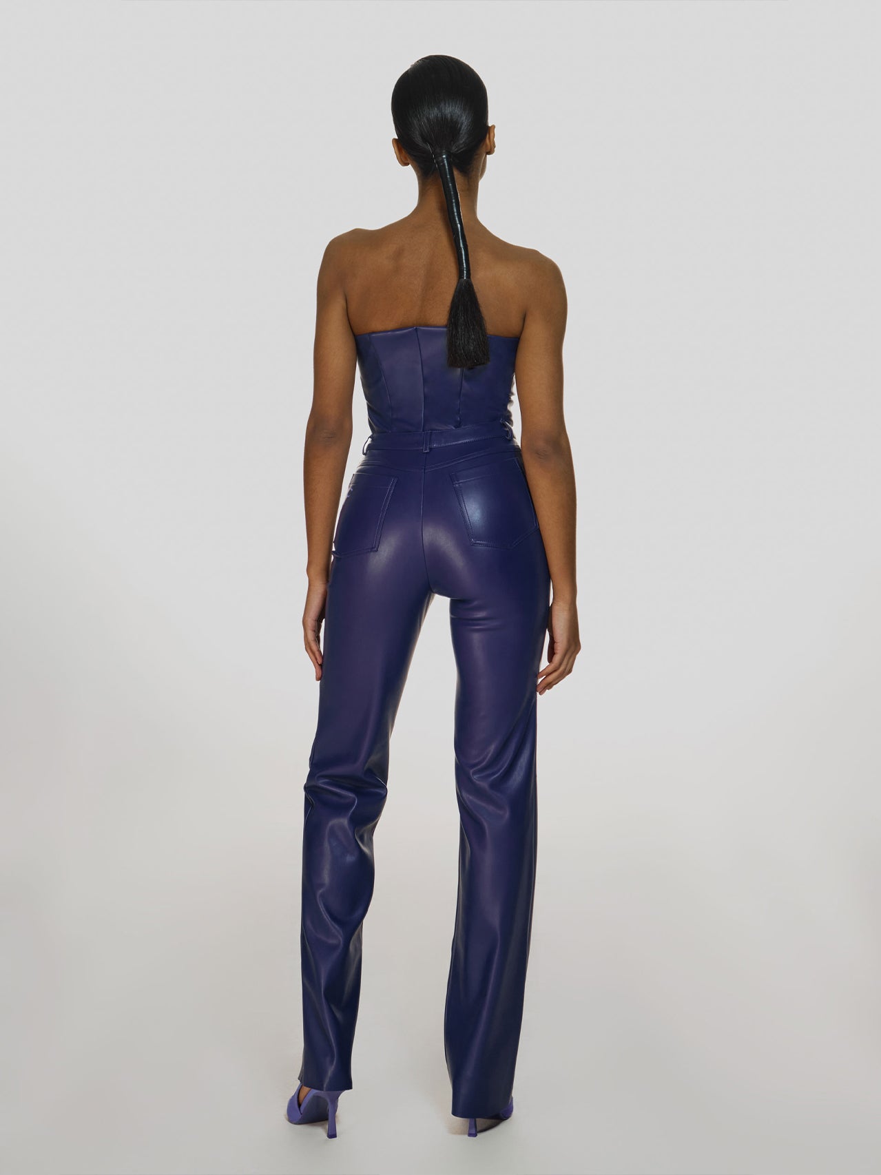 Full shot of a girl facing back in a purple vegan leather tube top and purple vegan leather high rise pants with straight leg