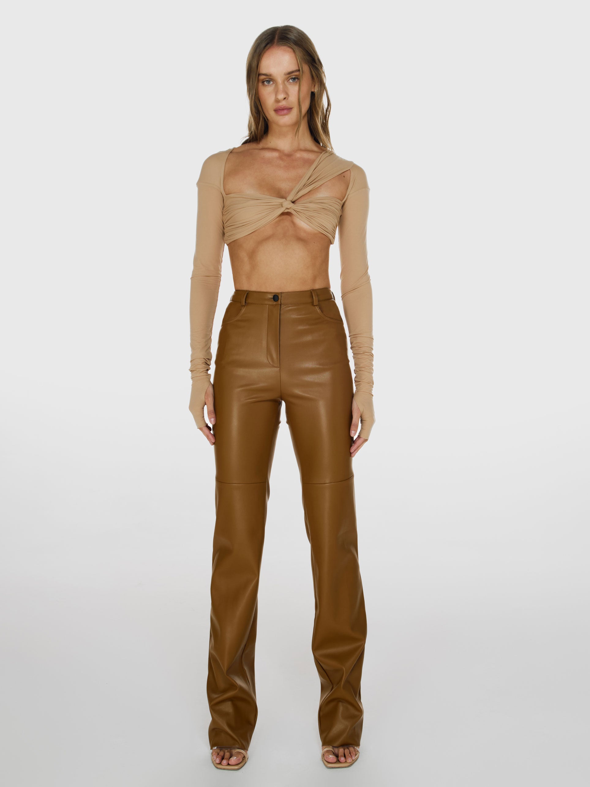 Full shot of a girl in a beige long sleeved crop top and brown vegan leather pants with straight leg