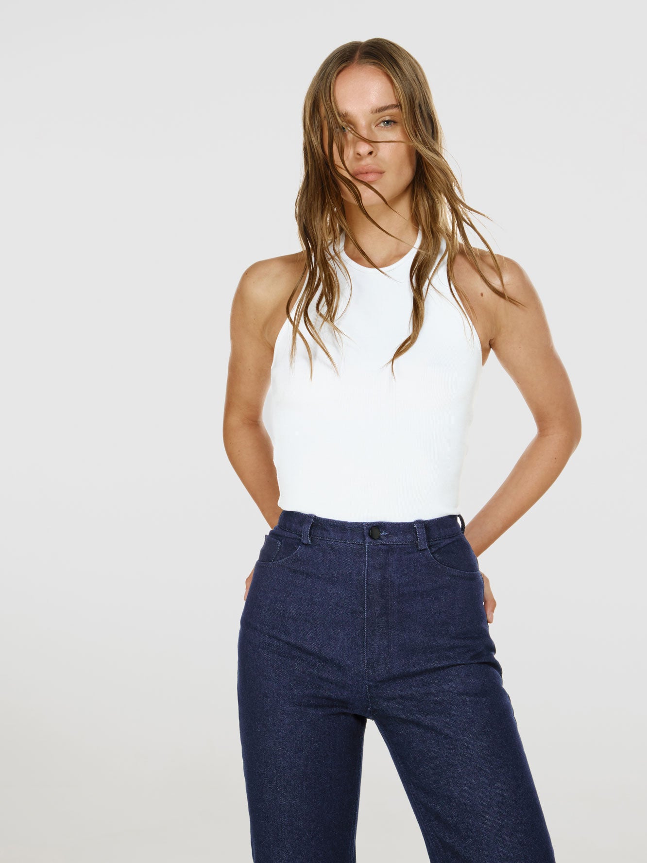 Cowboy shot of a girl in white viscose tank top and blue denim jeans