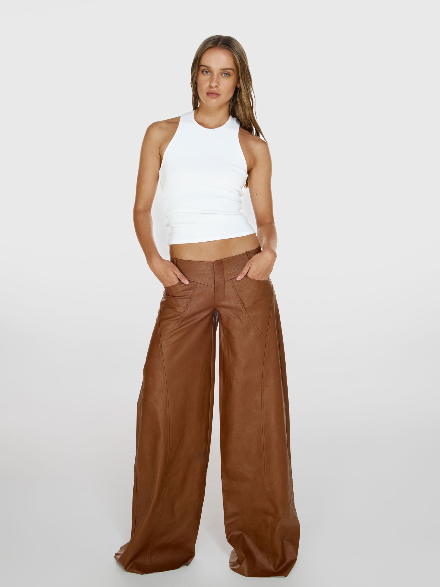 Full shot of a girl in a white viscose tank top and brown vegan leather low rise wide leg pants
