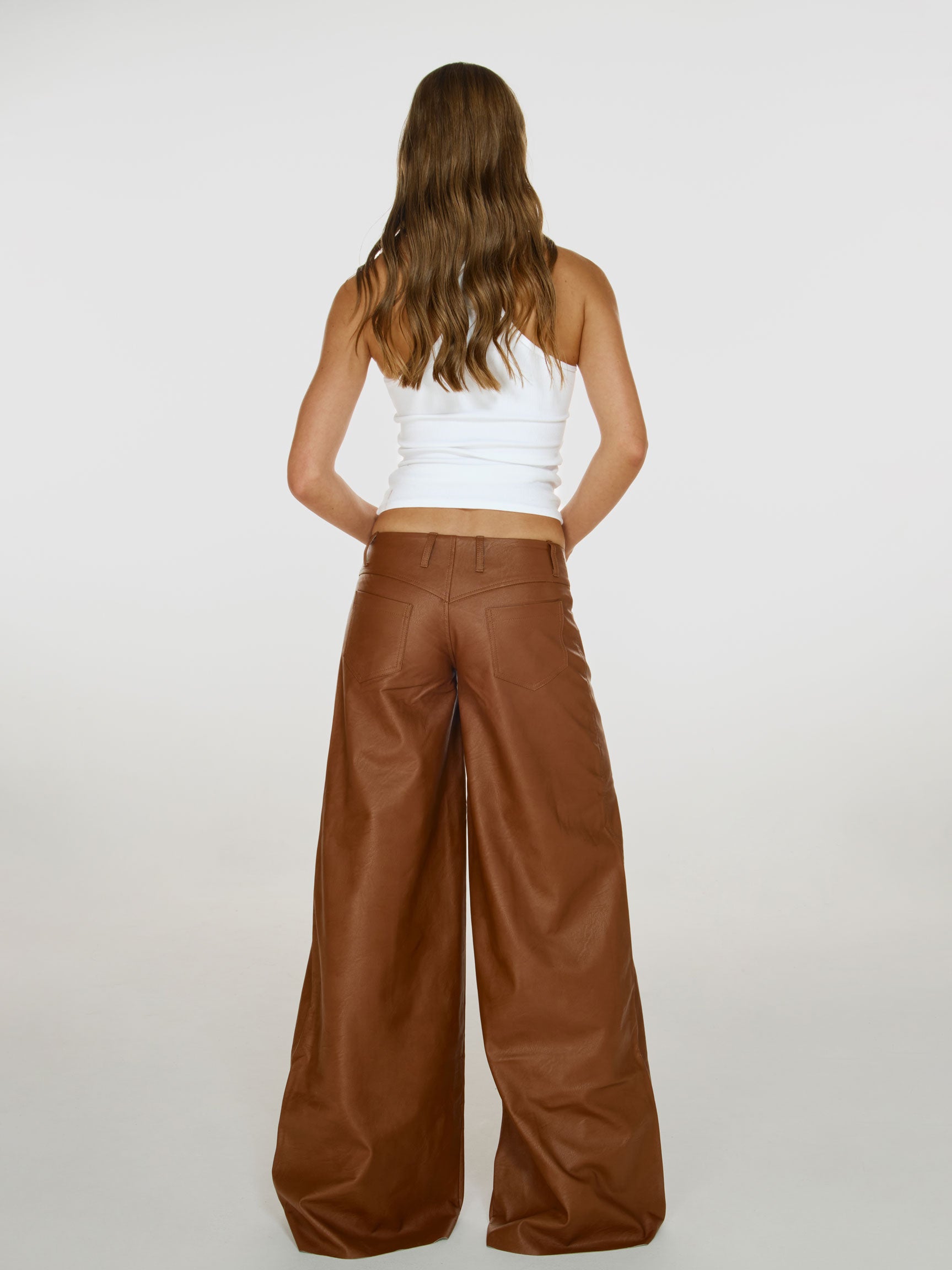 Full shot of a girl facing back in a white viscose tank top and brown vegan leather low rise wide leg pants