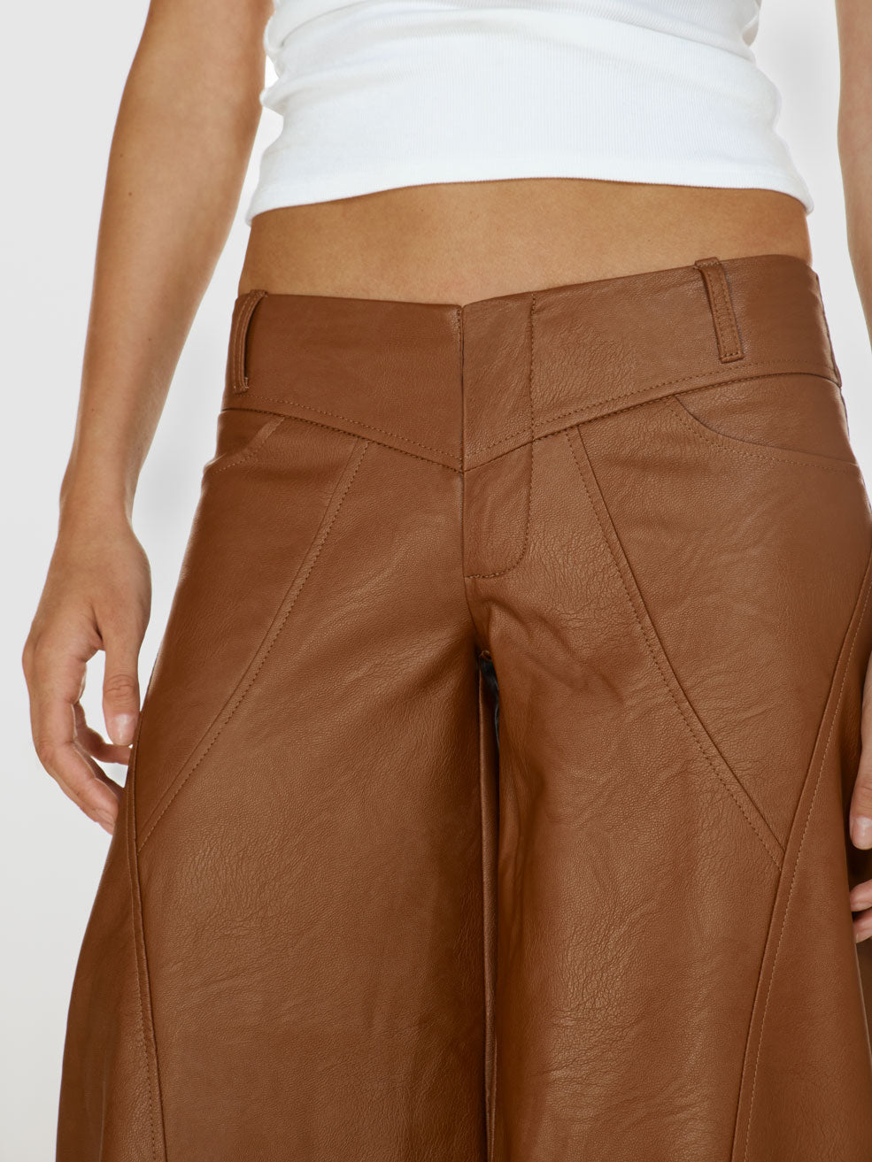 Closeup shot of a girl in a white viscose tank top and brown vegan leather low rise wide leg pants