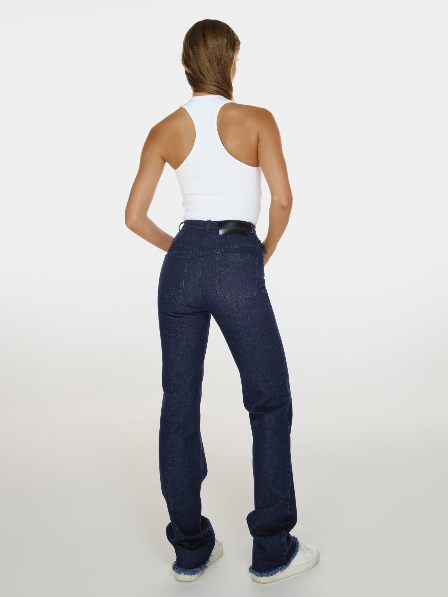 Full shot of a girl facing back in white cotton tank top and blue denim jeans