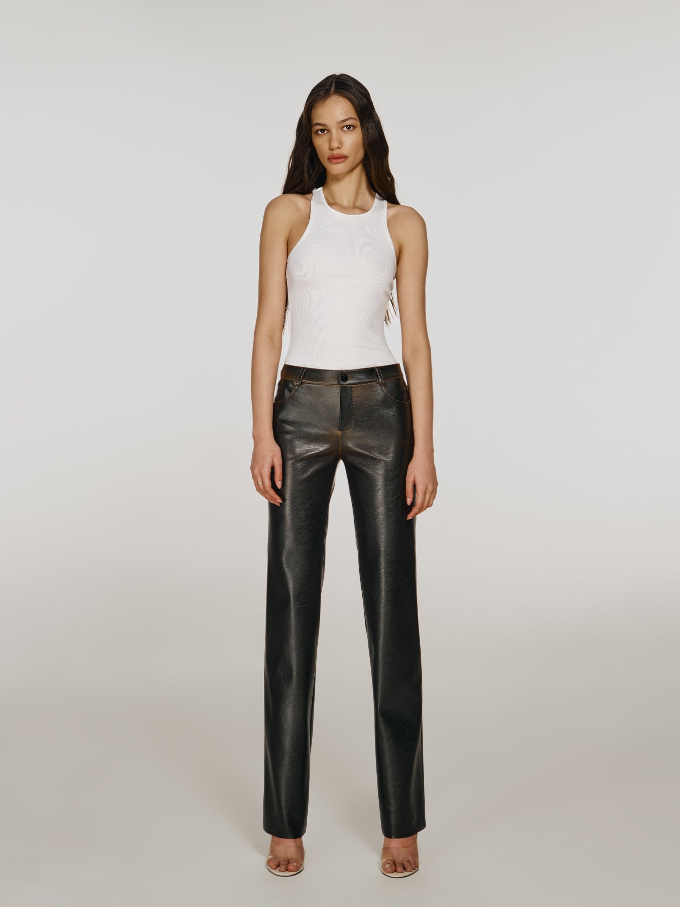Full shot of a girl in a white viscose tank top and brown vegan leather pants with mid rise