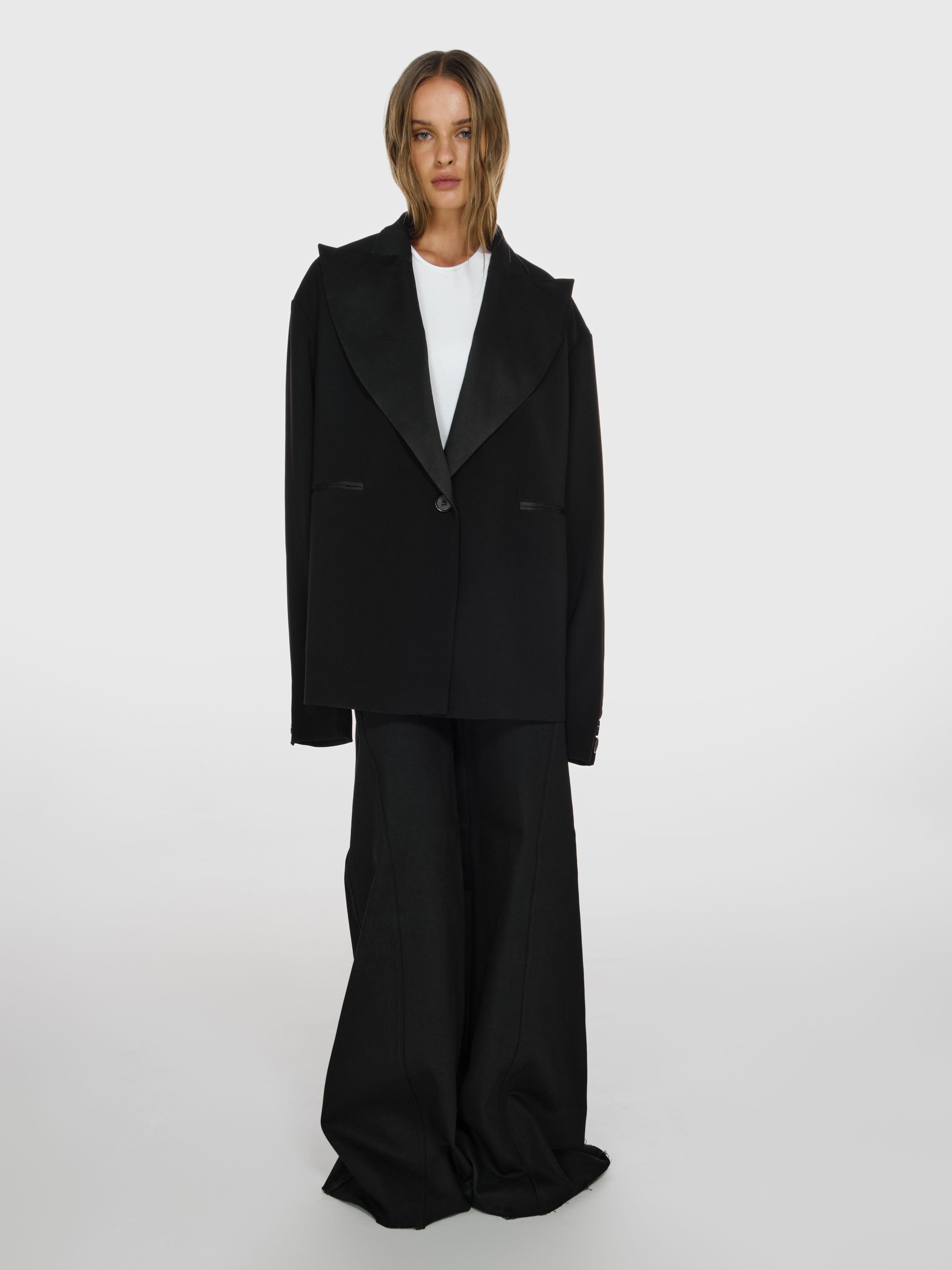 Full shot of a girl in a black oversized blazer, a white viscose tank top and black wide leg jeans