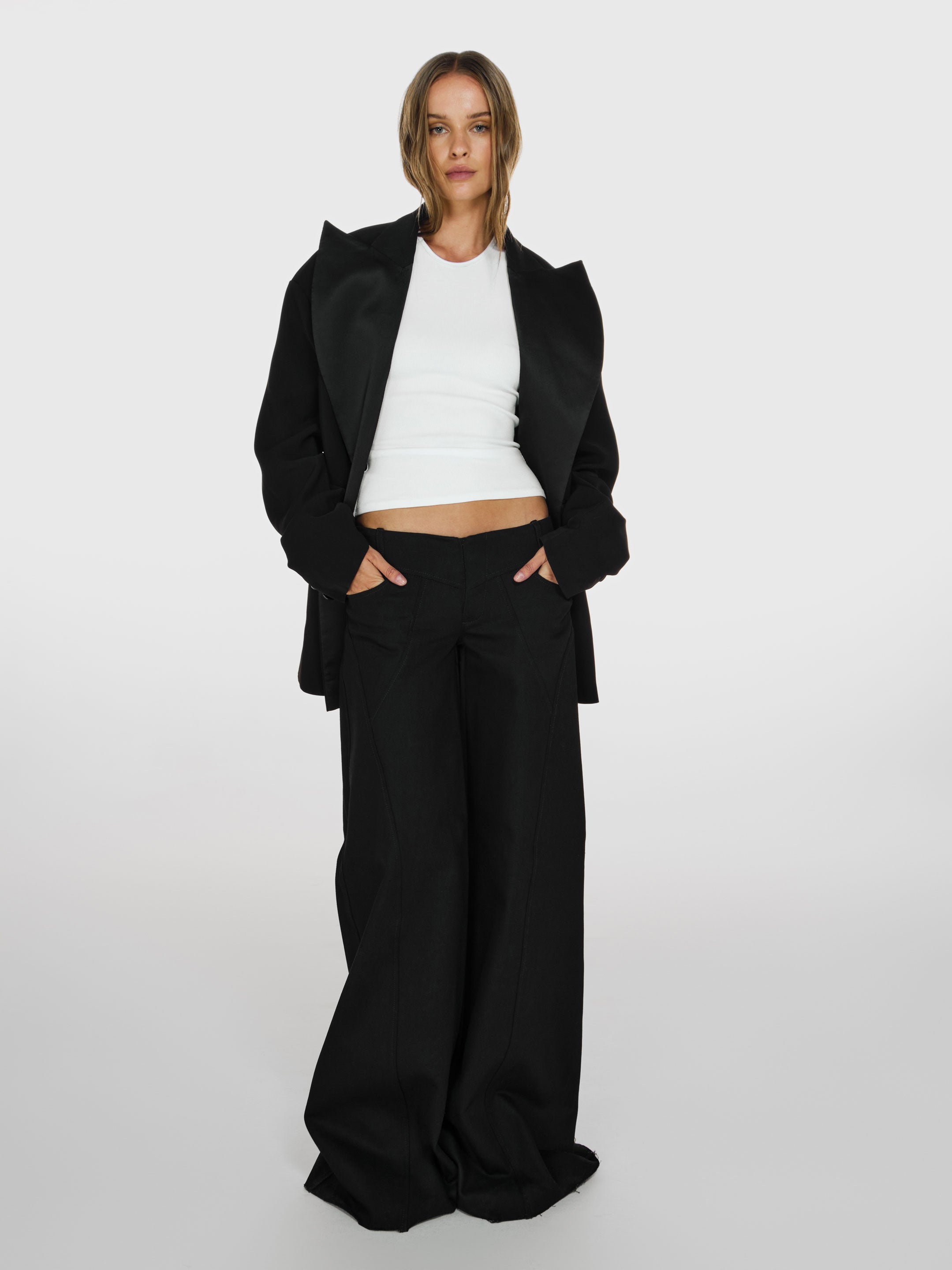 Full shot of a girl in a black oversized blazer, a white viscose tank top and black wide leg jeans
