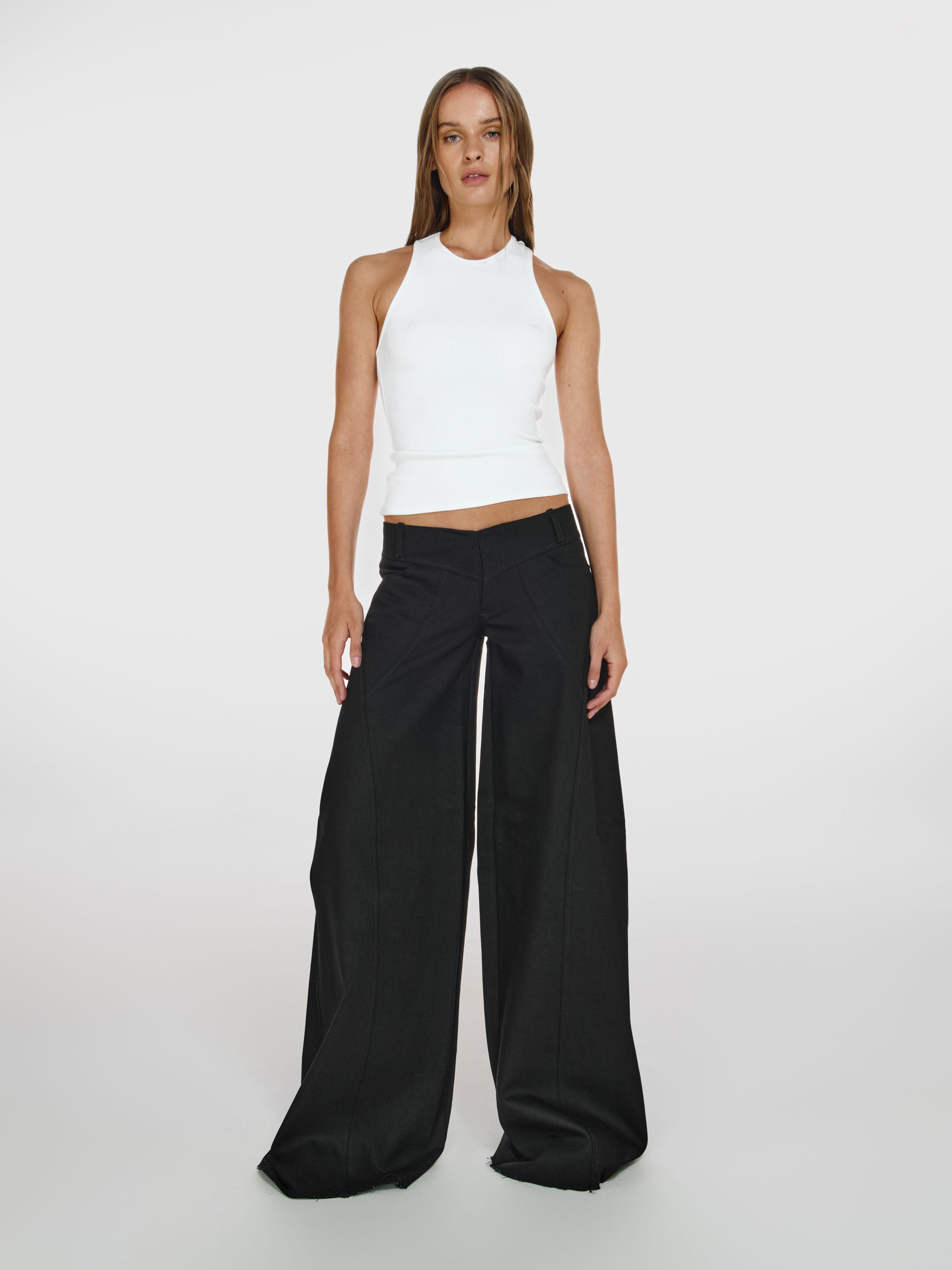 Full shot of a girl in a white viscose tank top and black wide leg jeans with low rise