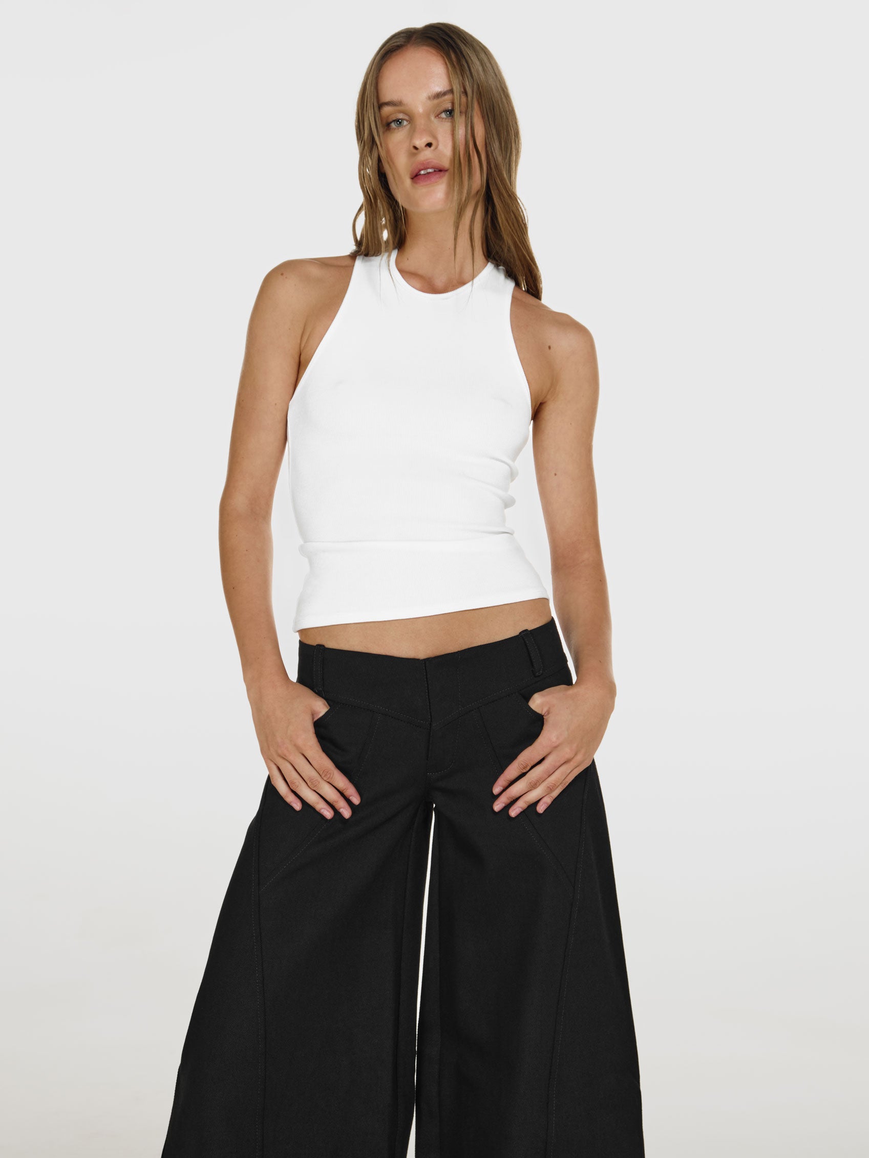 Medium full shot of a girl in a white viscose tank top and black wide leg jeans with low rise